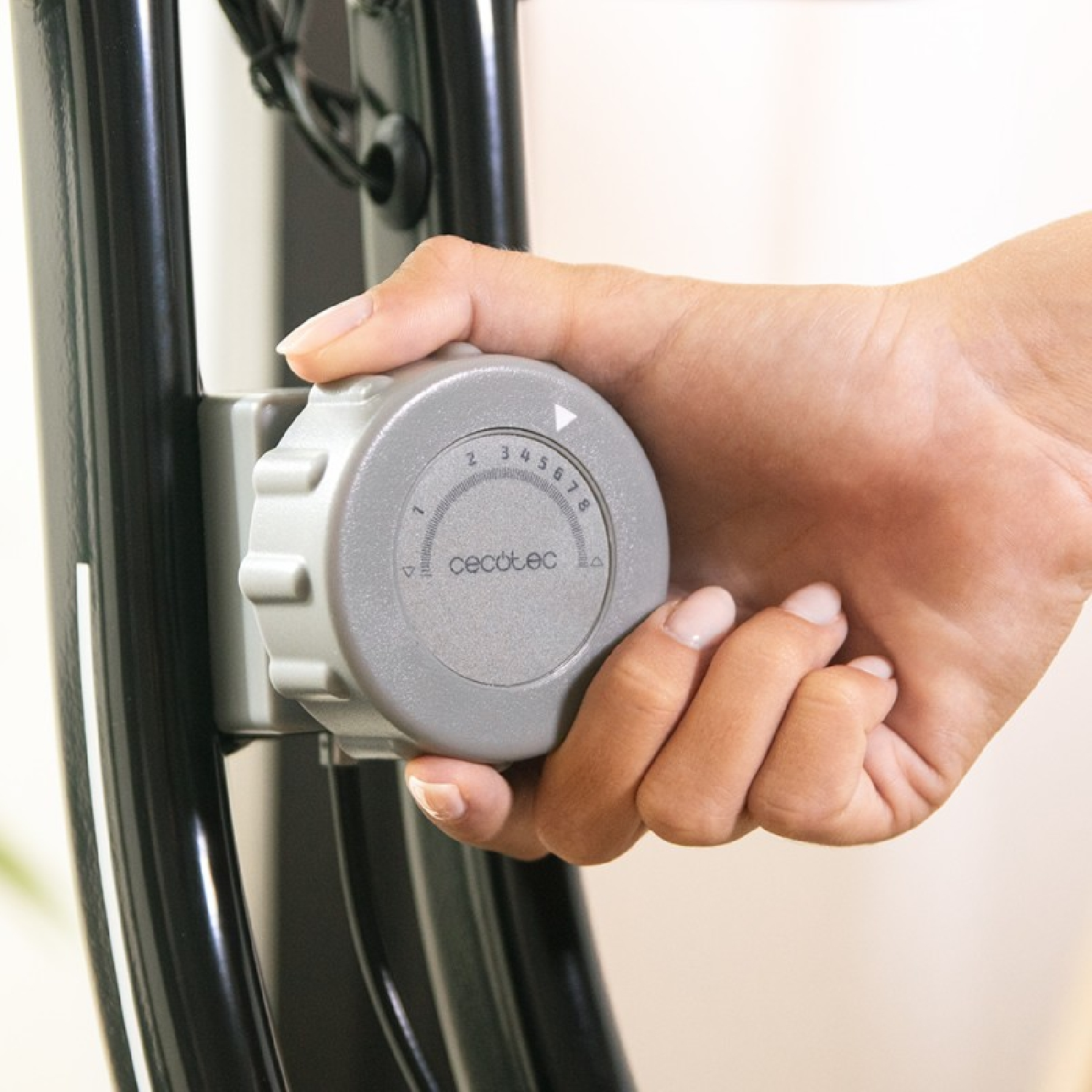 Mano girando un dial gris en una bicicleta de ejercicio negra. El dial tiene números del 1 al 8.