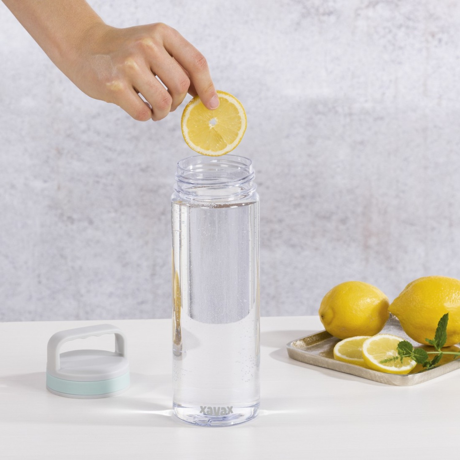 Hand fügt Zitronenscheibe einer Wasserflasche mit Zitronen und Minze hinzu.