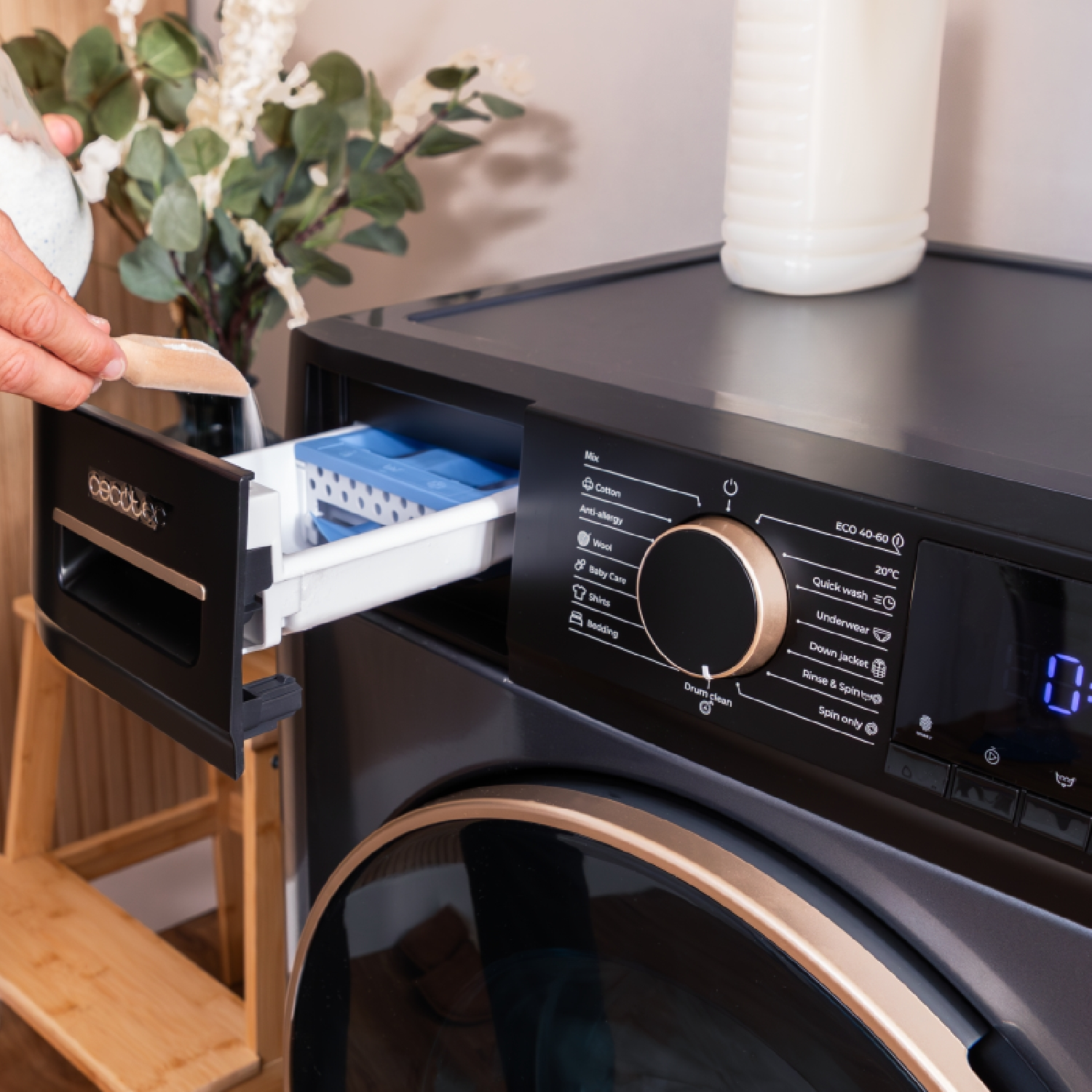 Osoba wlewa detergent do szuflady pralki, z butelką detergentu w tle.