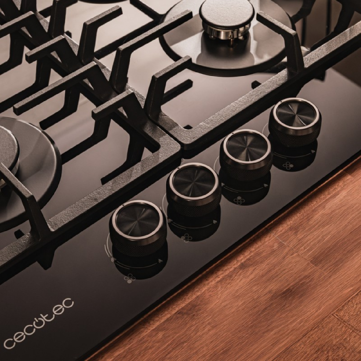 Zbliżenie czarnej płyty grzejnej z palnikami i pokrętłami. Pokrętła są metalowe.