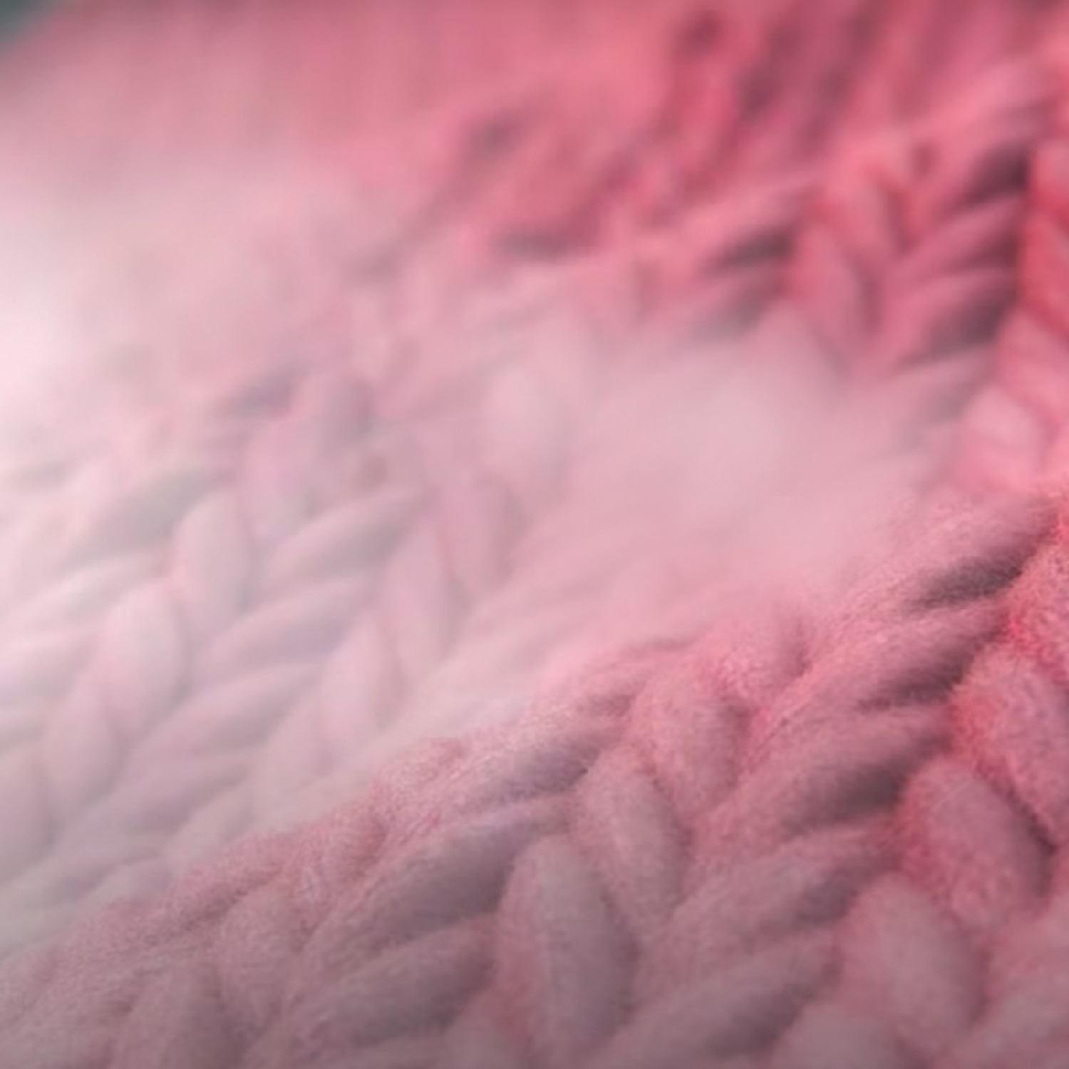 Zbliżenie na różowy, dziergany koc o miękkiej, rozmytym fakturze.