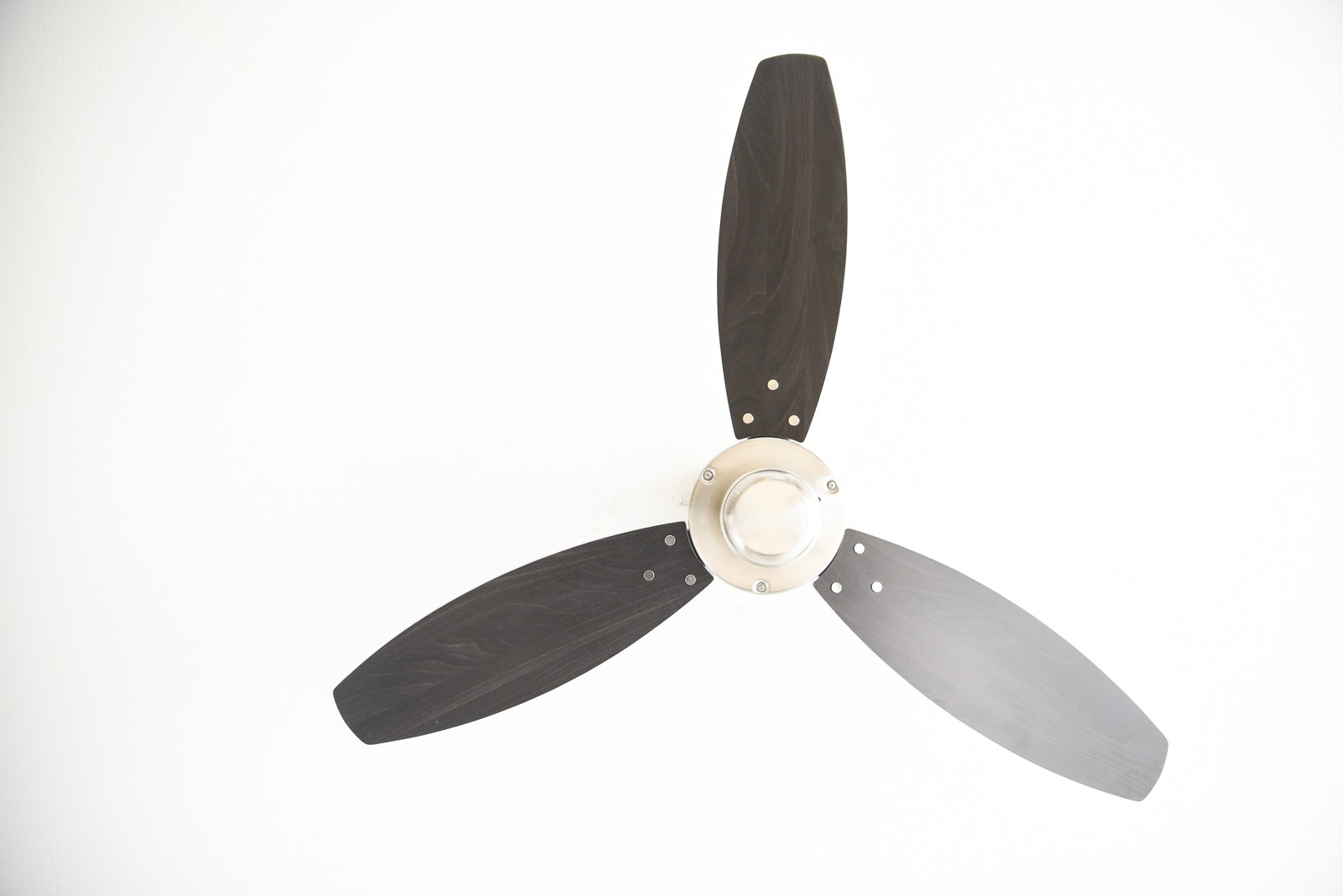 Deckenventilator mit drei Flügeln, silbernem Motor und dunkelgrauen Flügeln. Weißer Deckenhintergrund.