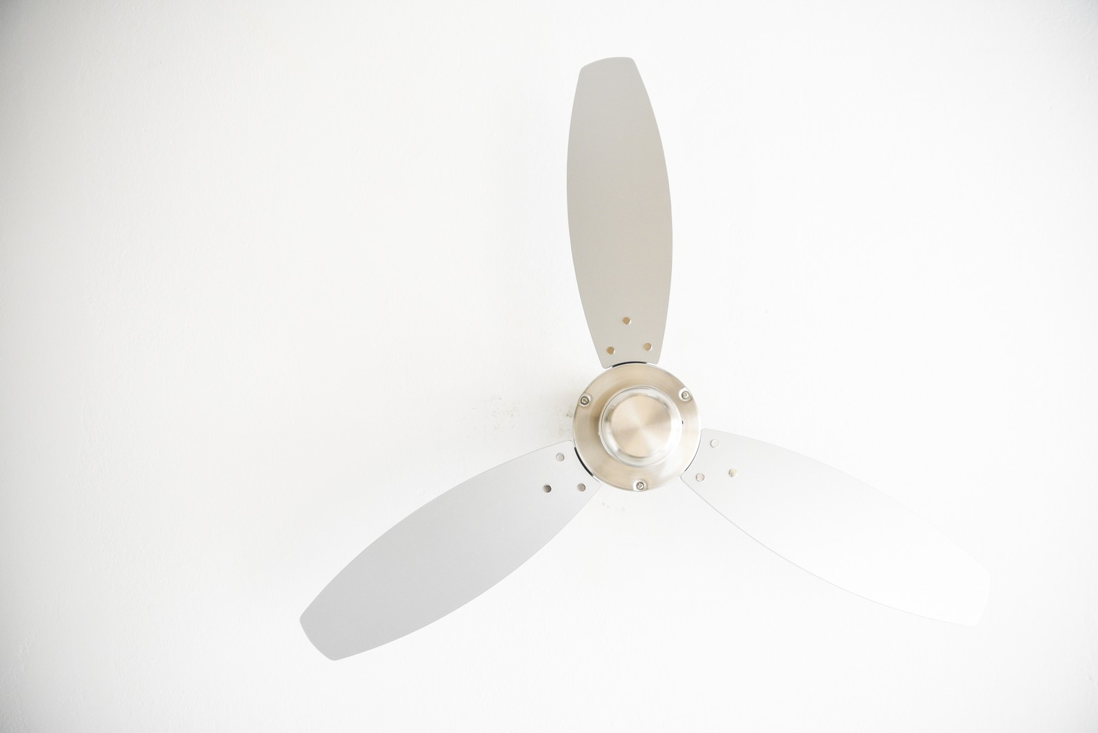 Deckenventilator mit drei silbernen Flügeln, silbernem Motor und weißem Deckenhintergrund.