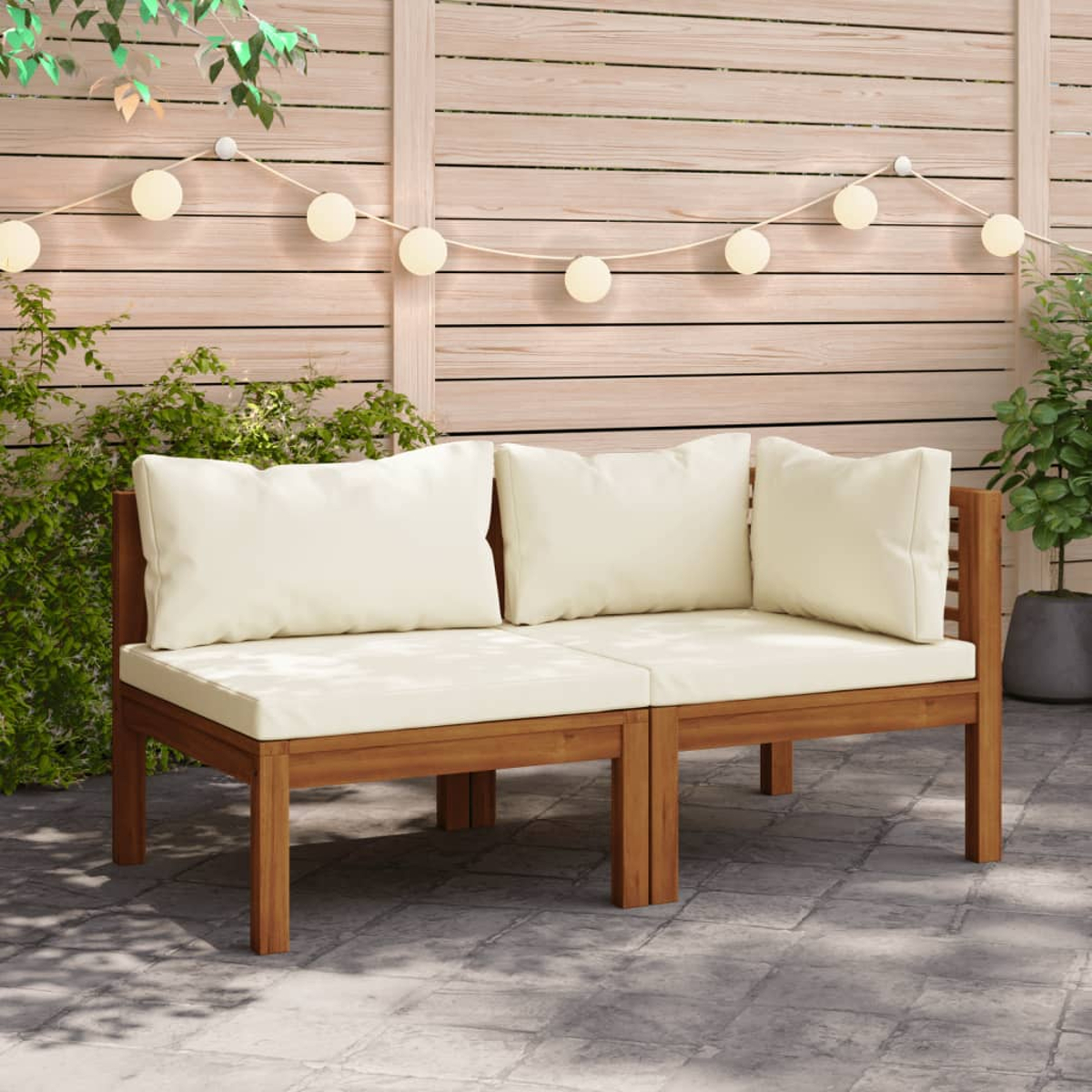 Outdoor-Holzsofa-Set mit weißen Kissen. Brauner Rahmen. Lichterketten und Pflanzen sind im Hintergrund.