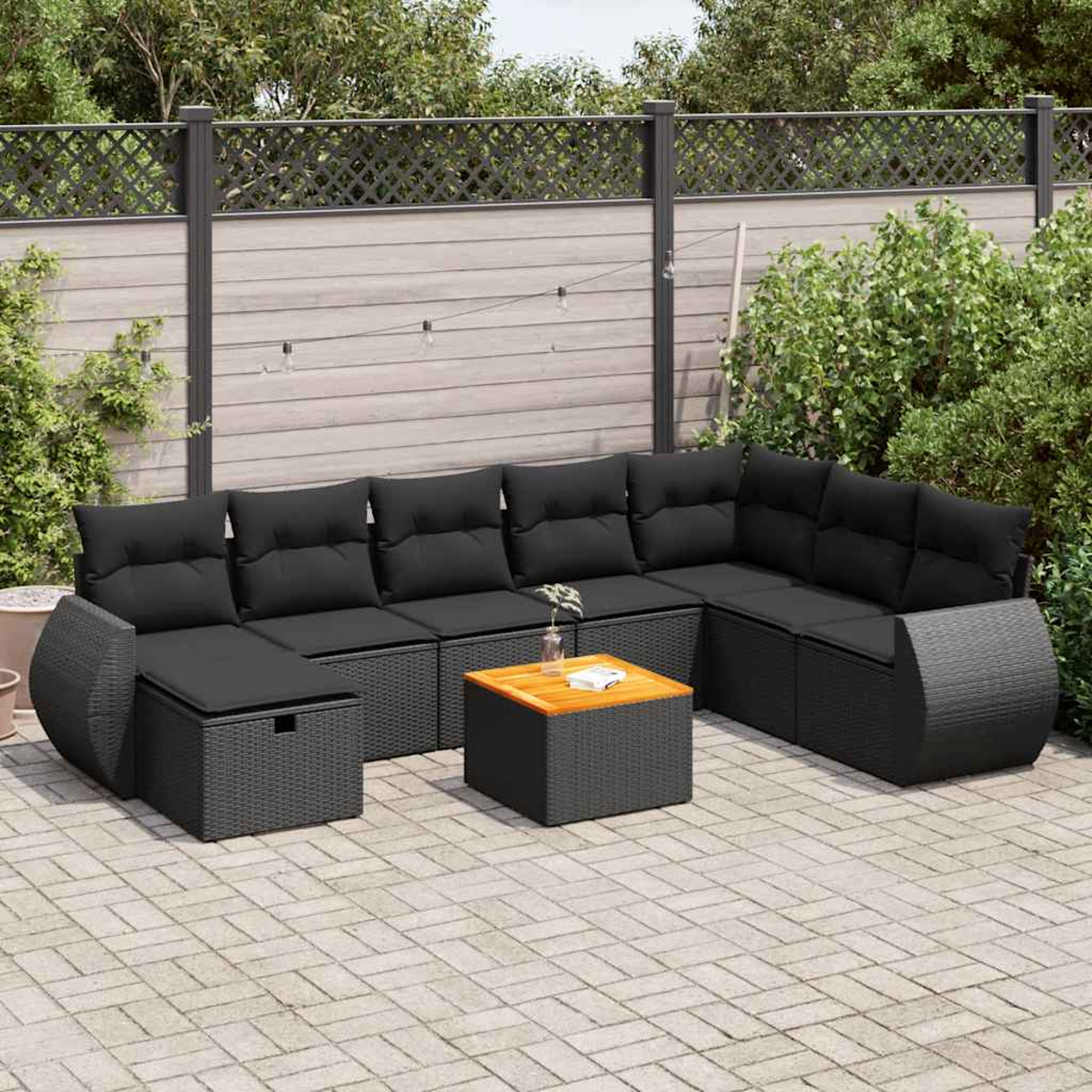 Un set da patio esterno: divano angolare in vimini grigio scuro, tavolo in legno e ambiente naturale.