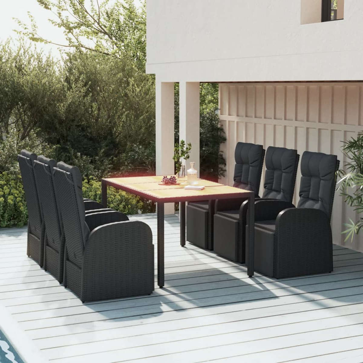 Essgruppe im Freien mit schwarzen Korbstühlen und Holztisch. Szene auf einer Terrasse. Pflanzen und Blumen sichtbar.