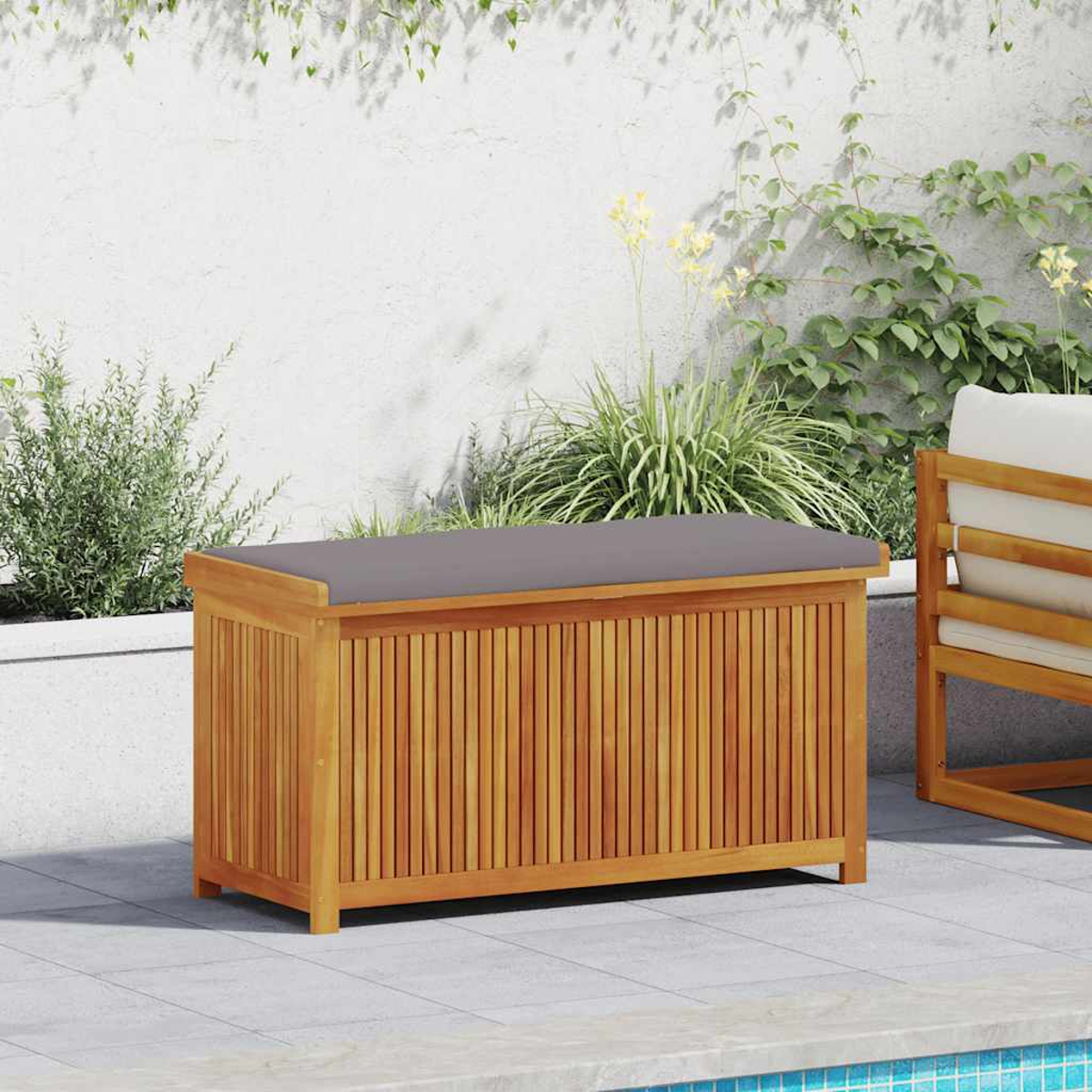 Holz-Stauraumbox mit grauem Kissen oben, auf einer Terrasse mit Blumen im Hintergrund.