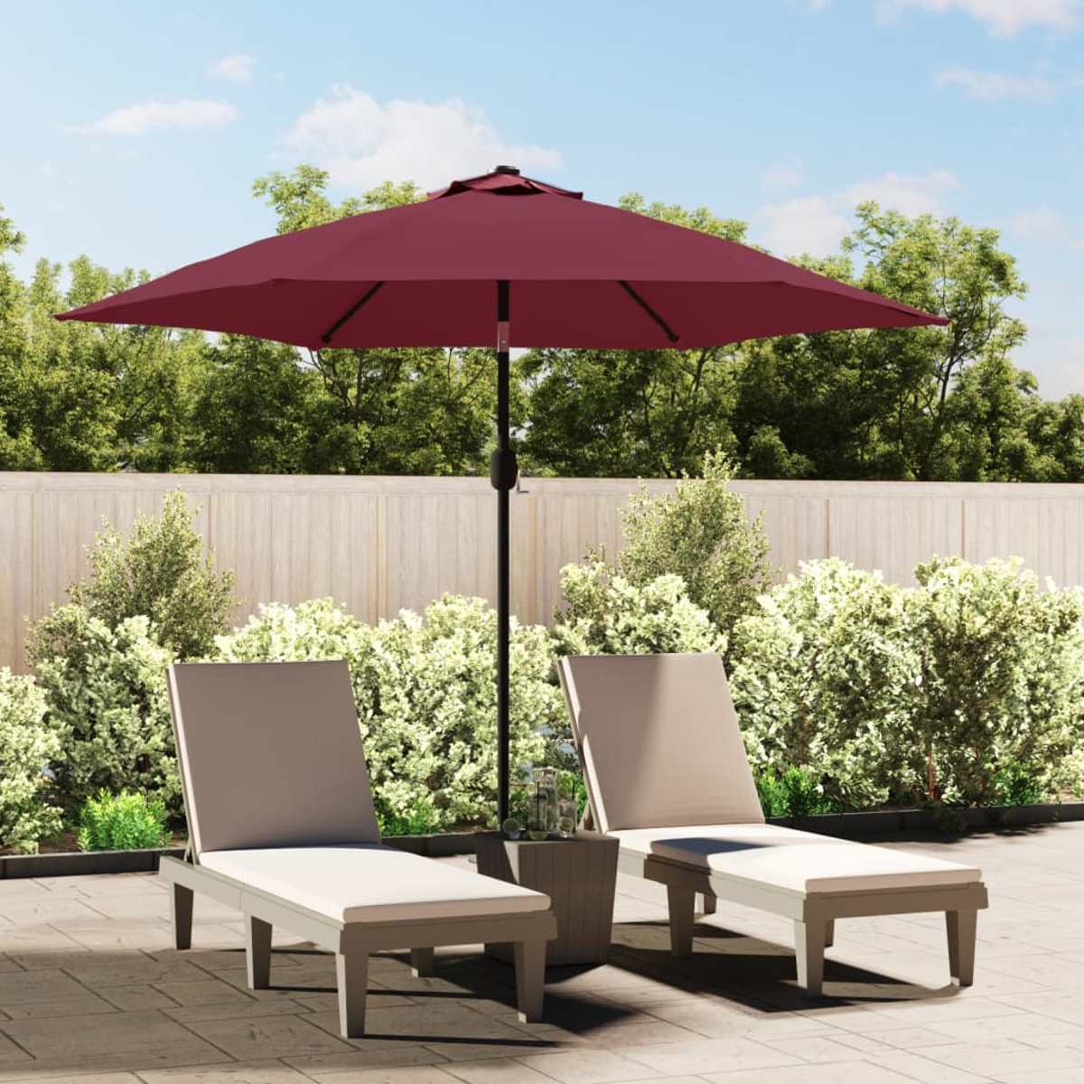 Zwei Liegestühle und ein weinroter Sonnenschirm auf einer Terrasse mit Laub im Hintergrund.