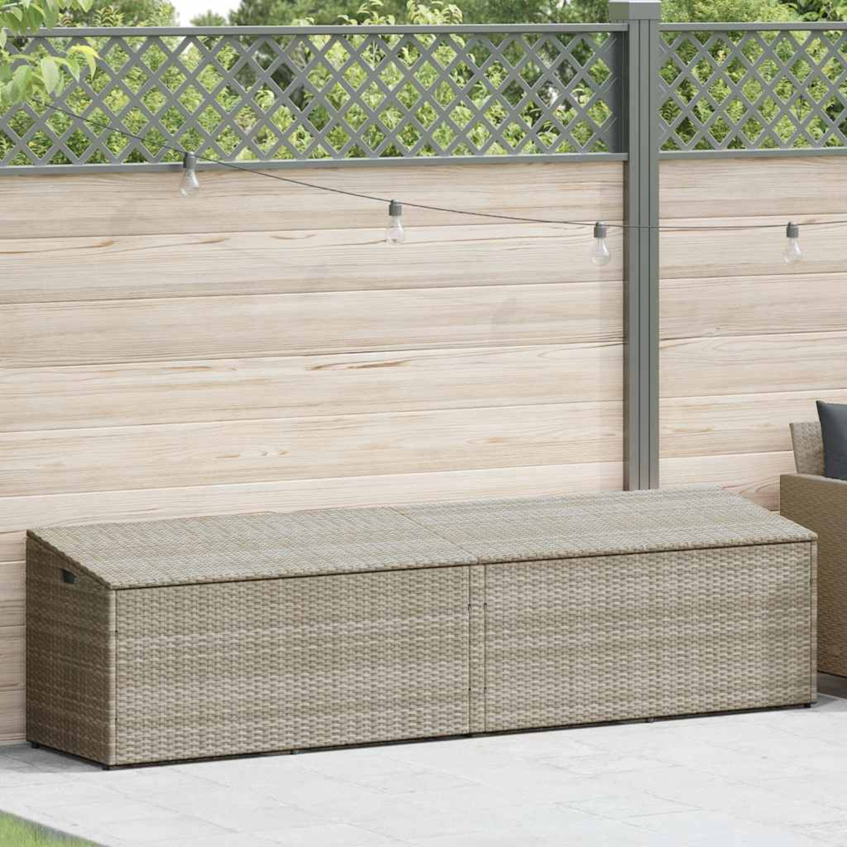 Eine beige Aufbewahrungsbank aus Korbgeflecht steht auf einer Terrasse. Im Hintergrund befindet sich ein Holzzaun mit Lichtern.