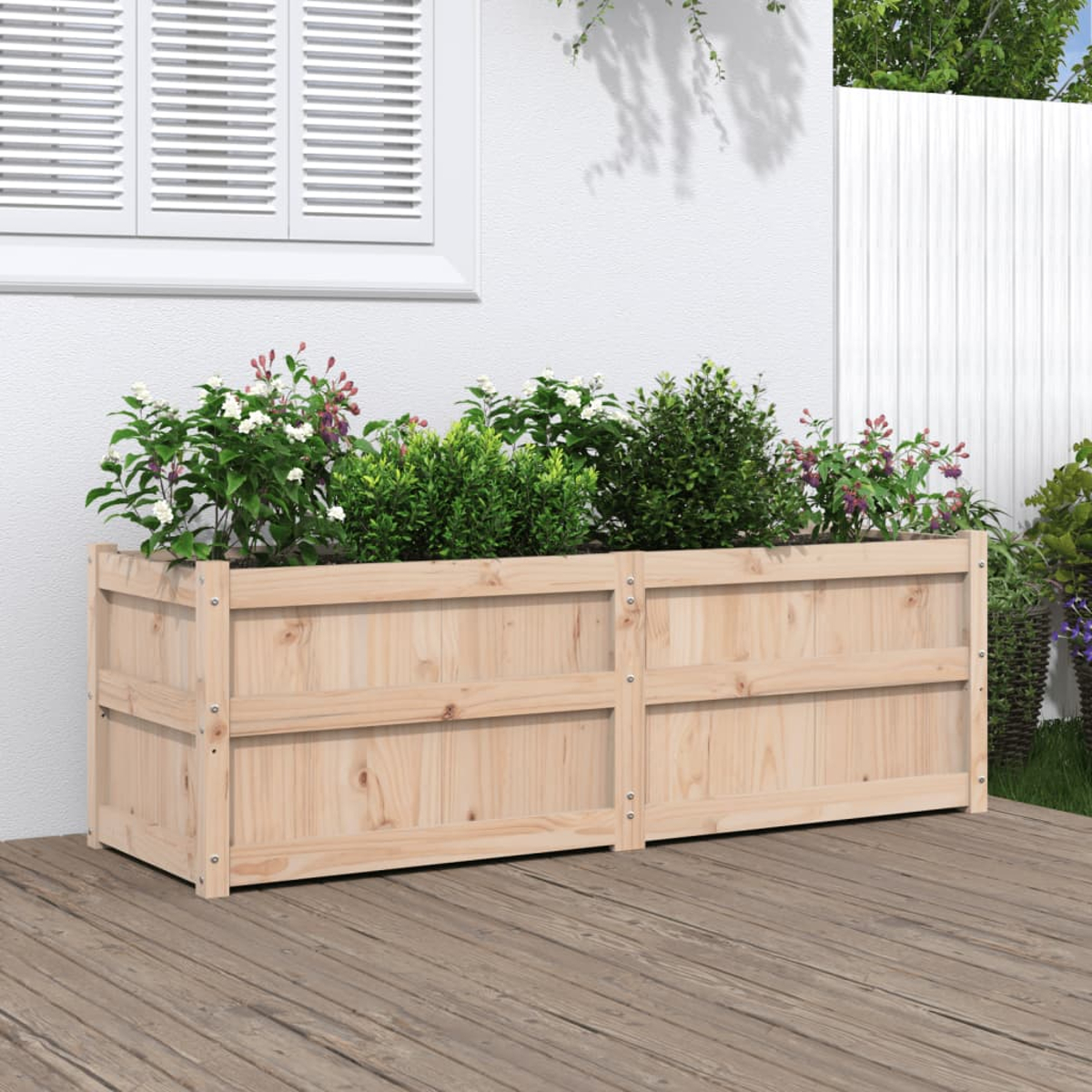Holzpflanzkasten mit Pflanzen und Blumen. Es steht auf einem Holzdeck mit einer weißen Wand im Hintergrund.