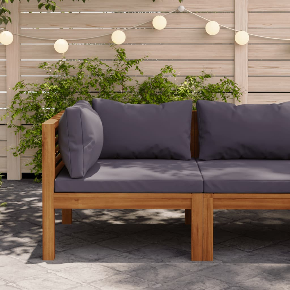 Ecksofa aus Holz für den Außenbereich mit grauen Kissen. Im Hintergrund sind ein Holzzaun und Pflanzen zu sehen.