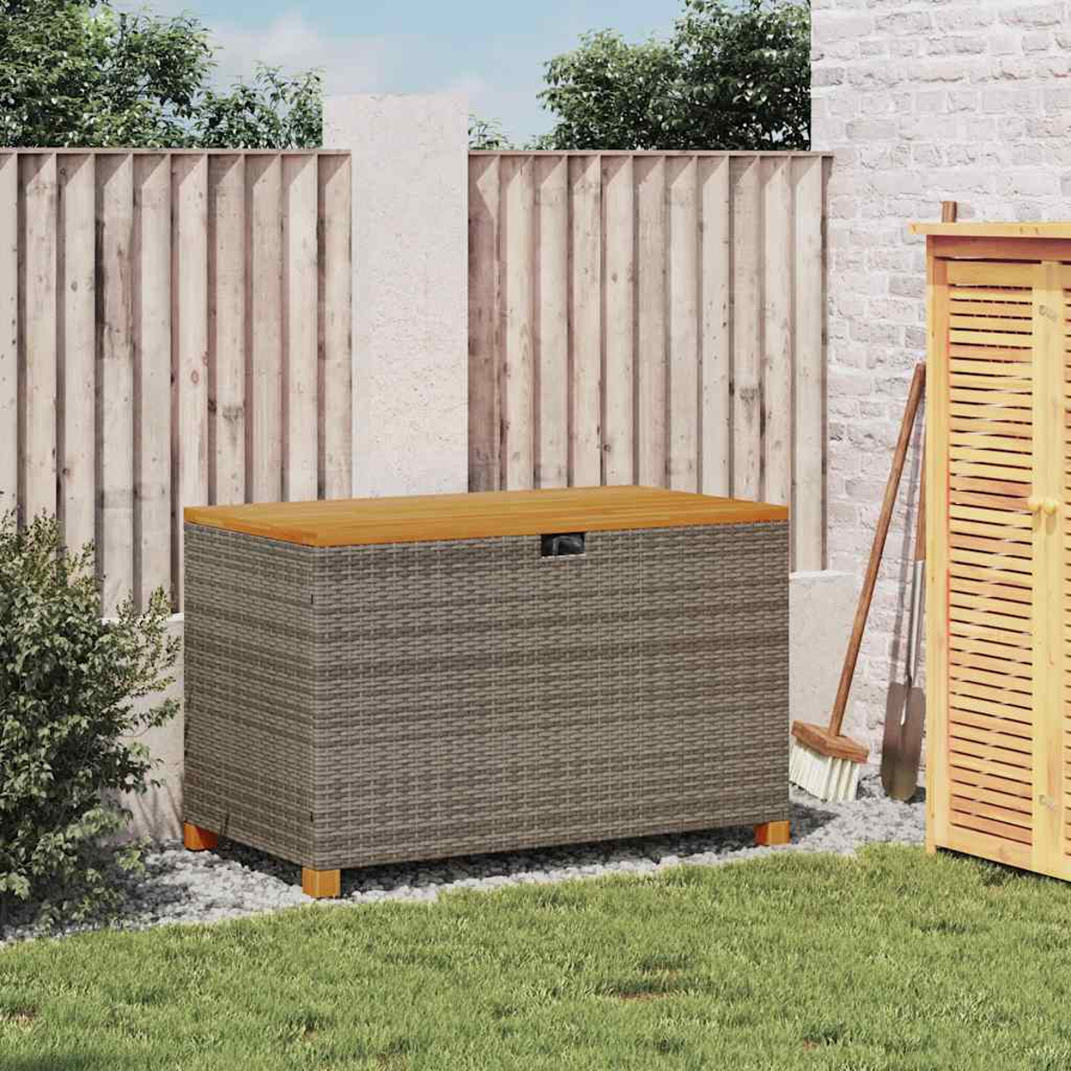 Eine Aufbewahrungsbox aus Korbgeflecht mit Holzdeckel, platziert in einem Garten. Im Hintergrund sind ein Zaun und Gras zu sehen.