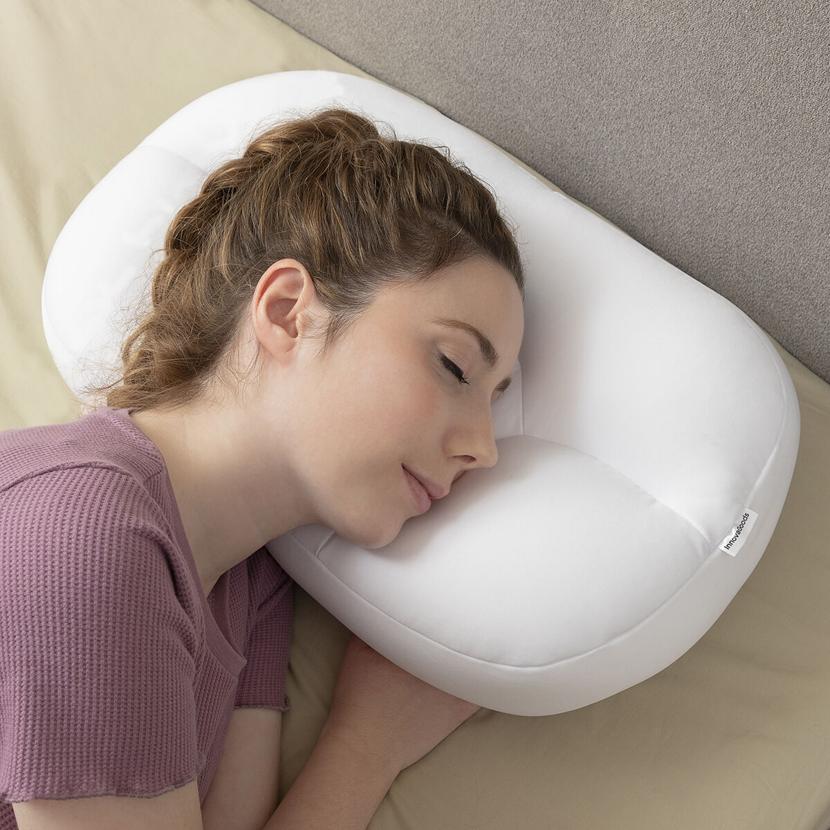 Una donna dorme su un cuscino bianco, indossa una camicia rosa, con un'illuminazione soffusa.