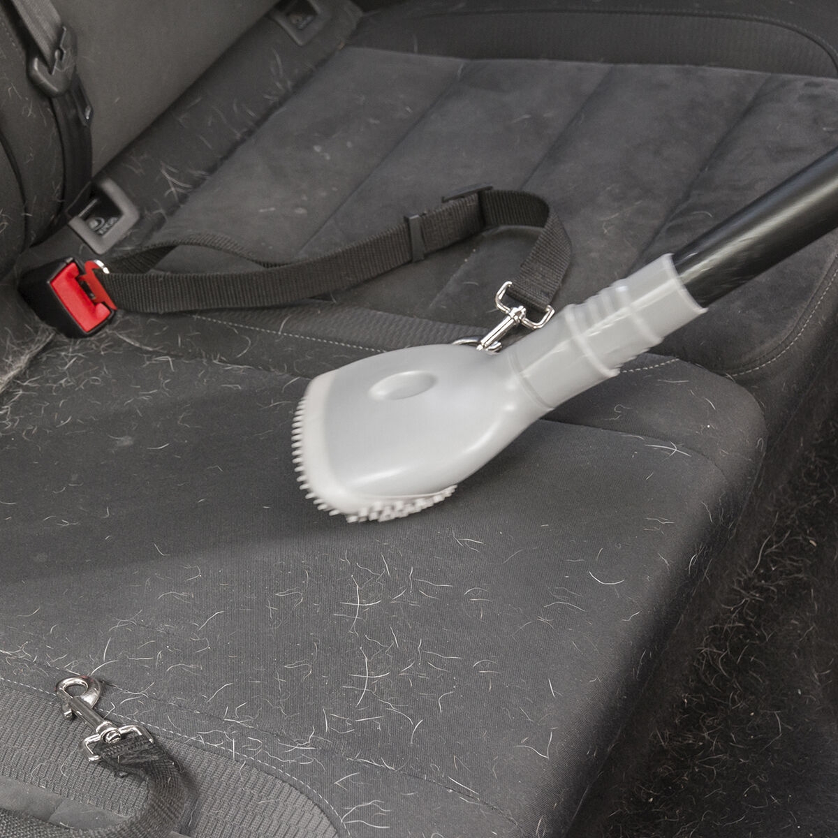 Graues Polsterwerkzeug entfernt Tierhaare von einem schwarzen Autositz mit Sicherheitsgurt.