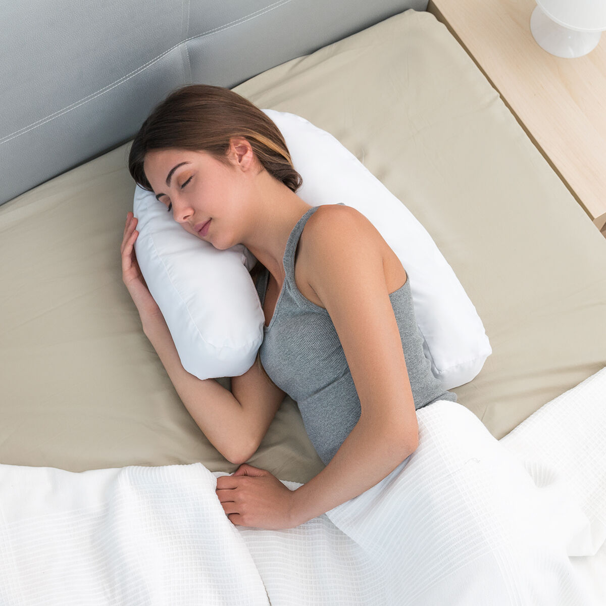 Draufsicht einer Frau, die auf einem weißen U-förmigen Kissen auf einem hellbraunen Bett schläft.