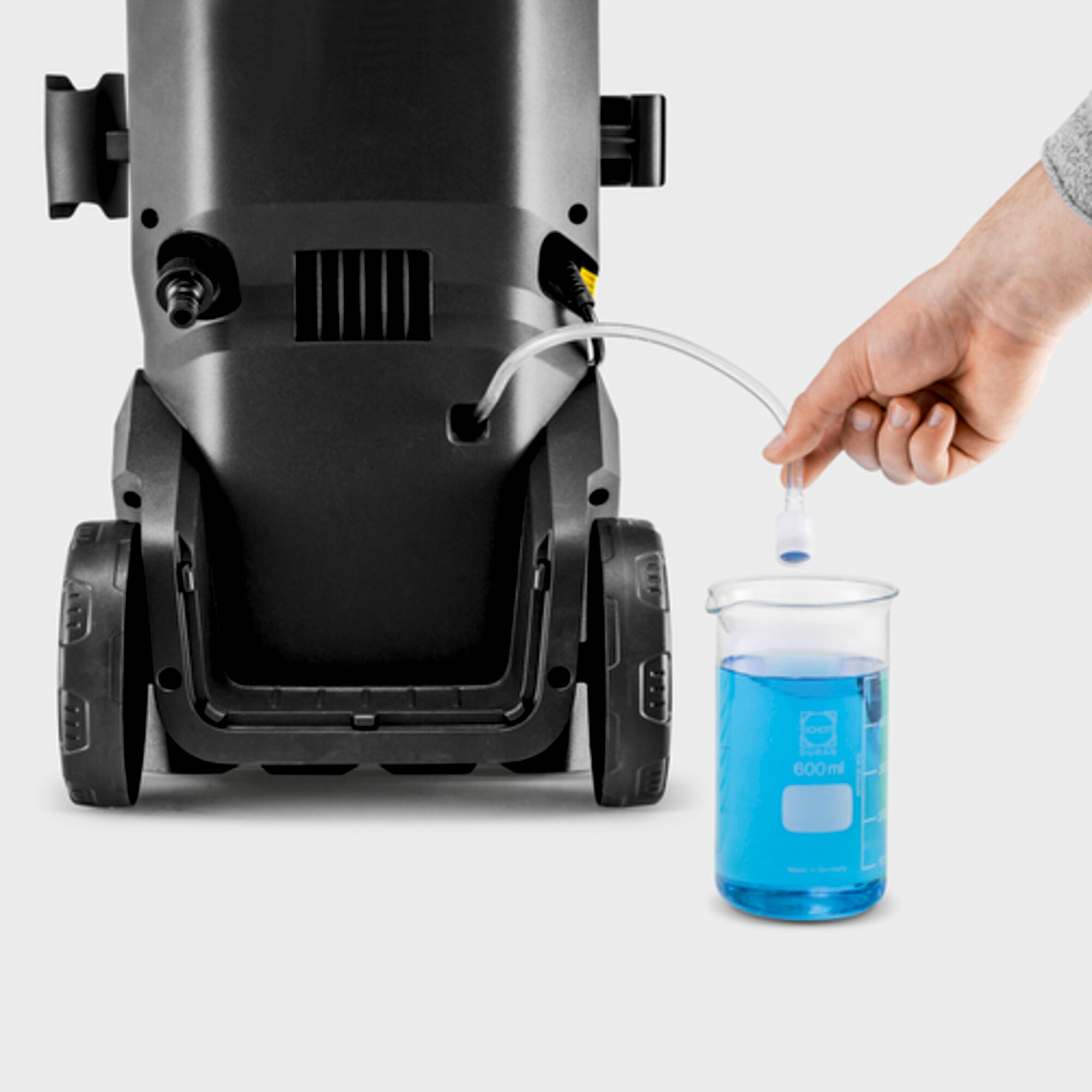 Ręka dodająca płyn czyszczący do zlewki, w pobliżu myjki ciśnieniowej.