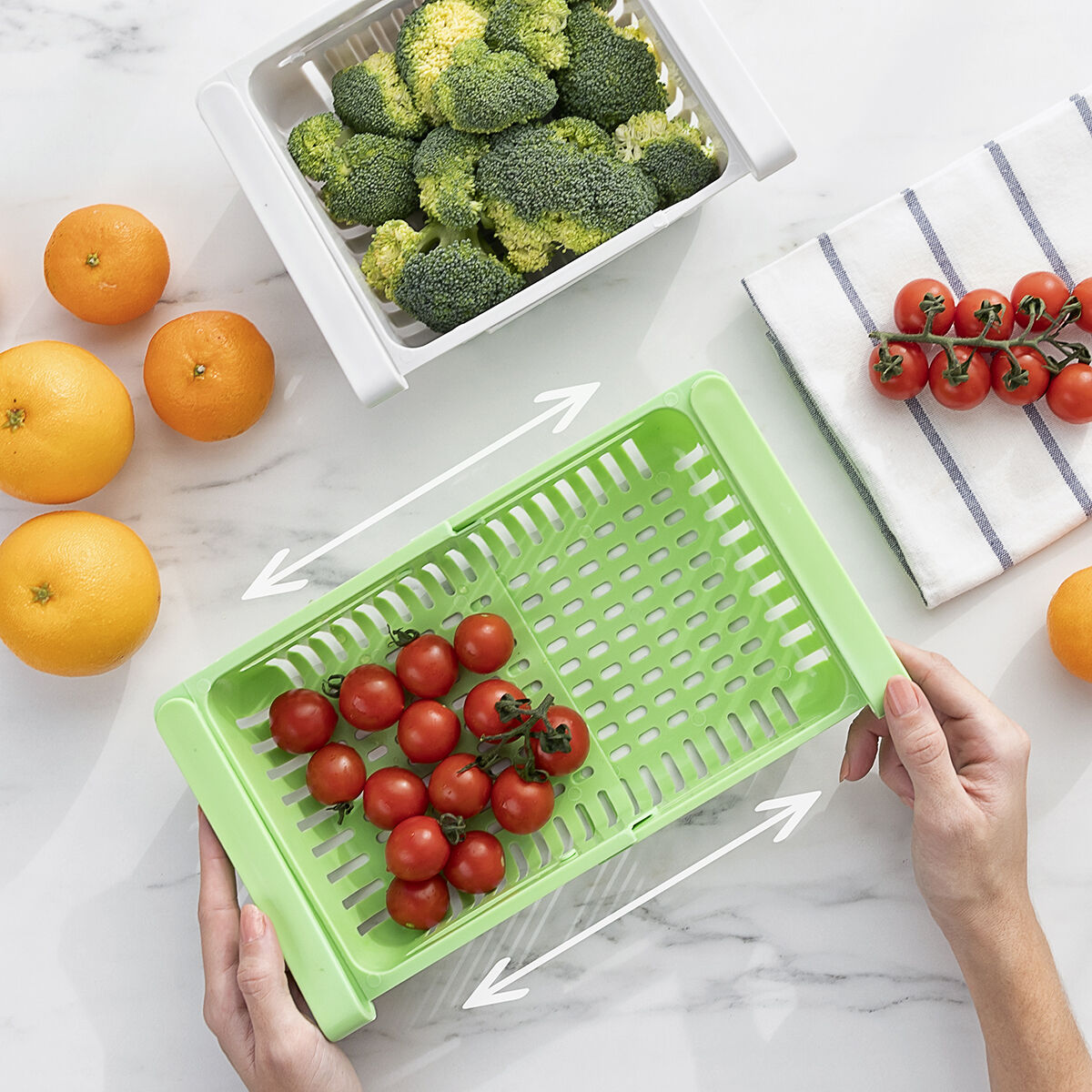 Ein Tablett mit Tomaten wird gefüllt, Brokkoli in einem anderen Tablett und Orangen auf weißer Oberfläche.