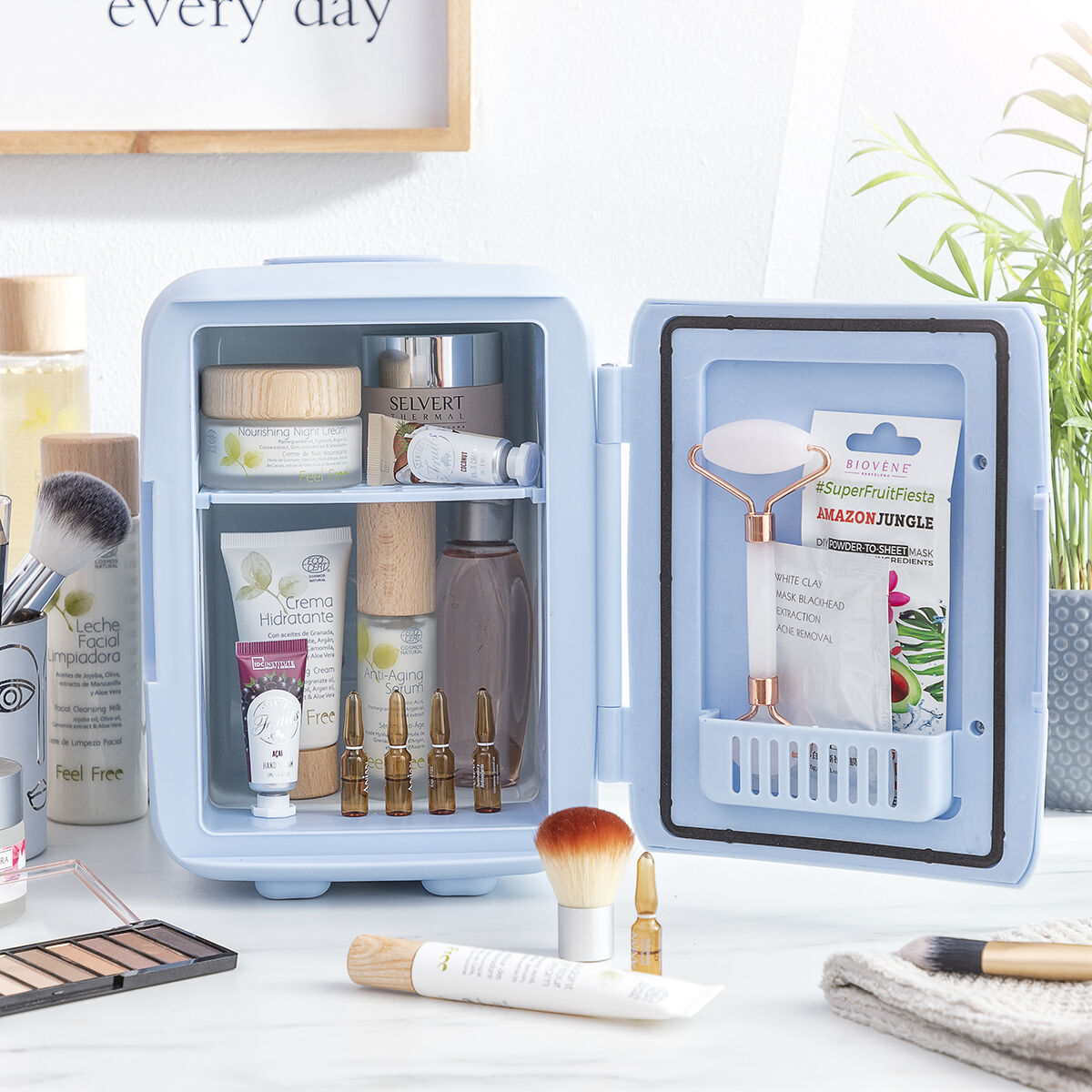 Un pequeño refrigerador azul claro con productos para el cuidado de la piel y maquillaje dentro, abierto sobre una mesa.