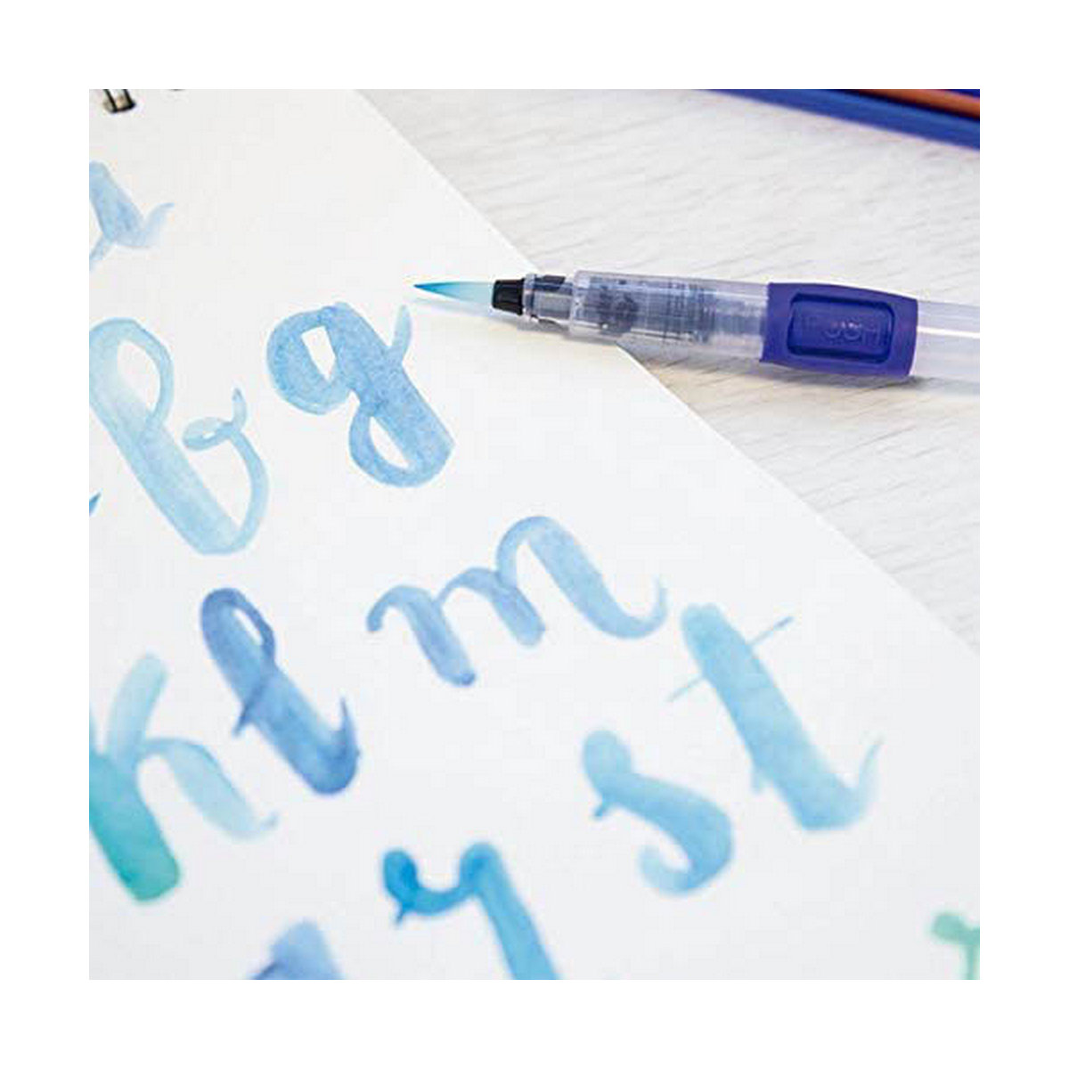 Nahaufnahme eines Wasserpinsels, der blaue Buchstaben auf eine weiße Seite schreibt. Die Buchstaben sind kursiv.