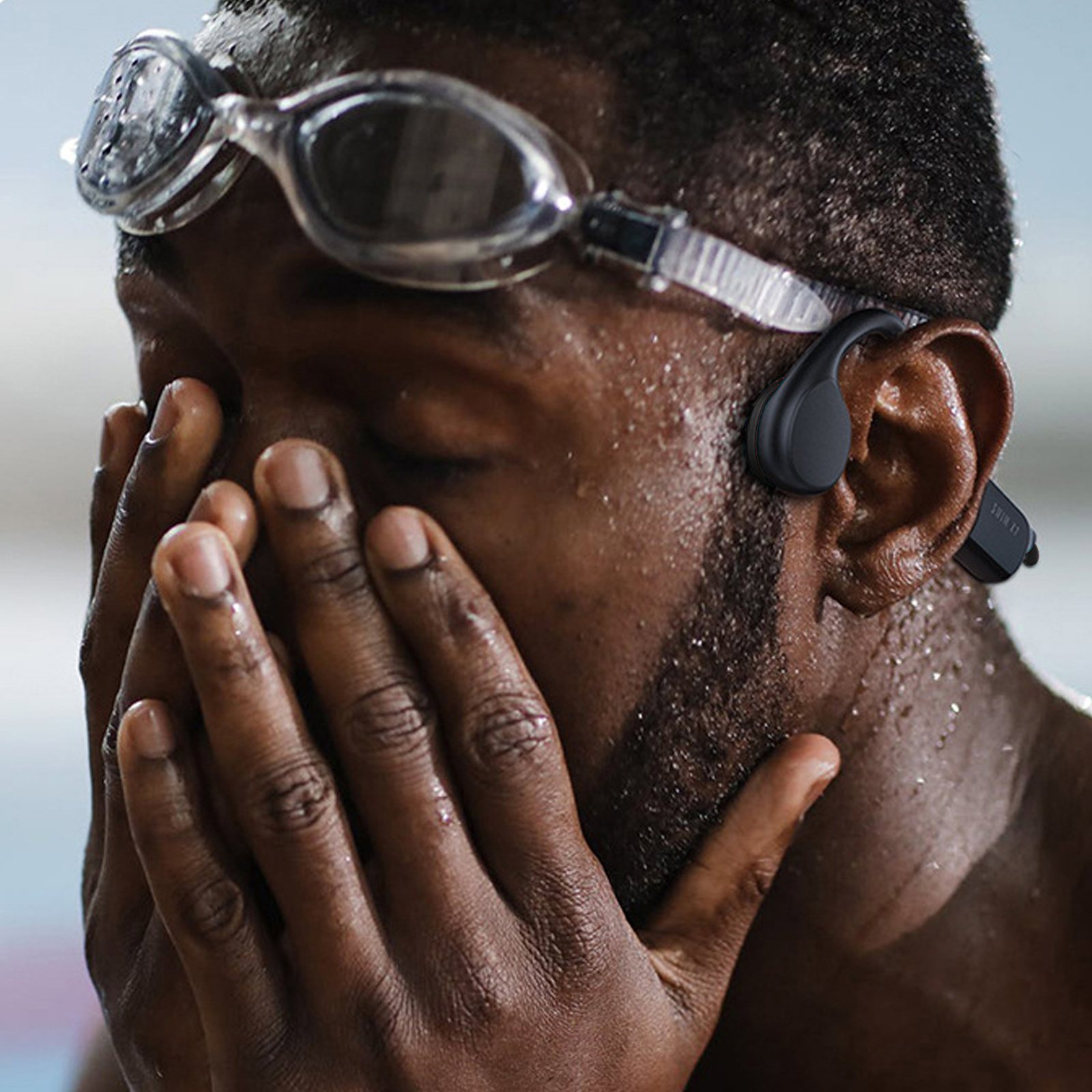 Mann mit Schwimmbrille und Ohrhörern, der sich das Gesicht hält. Er ist im Wasser.
