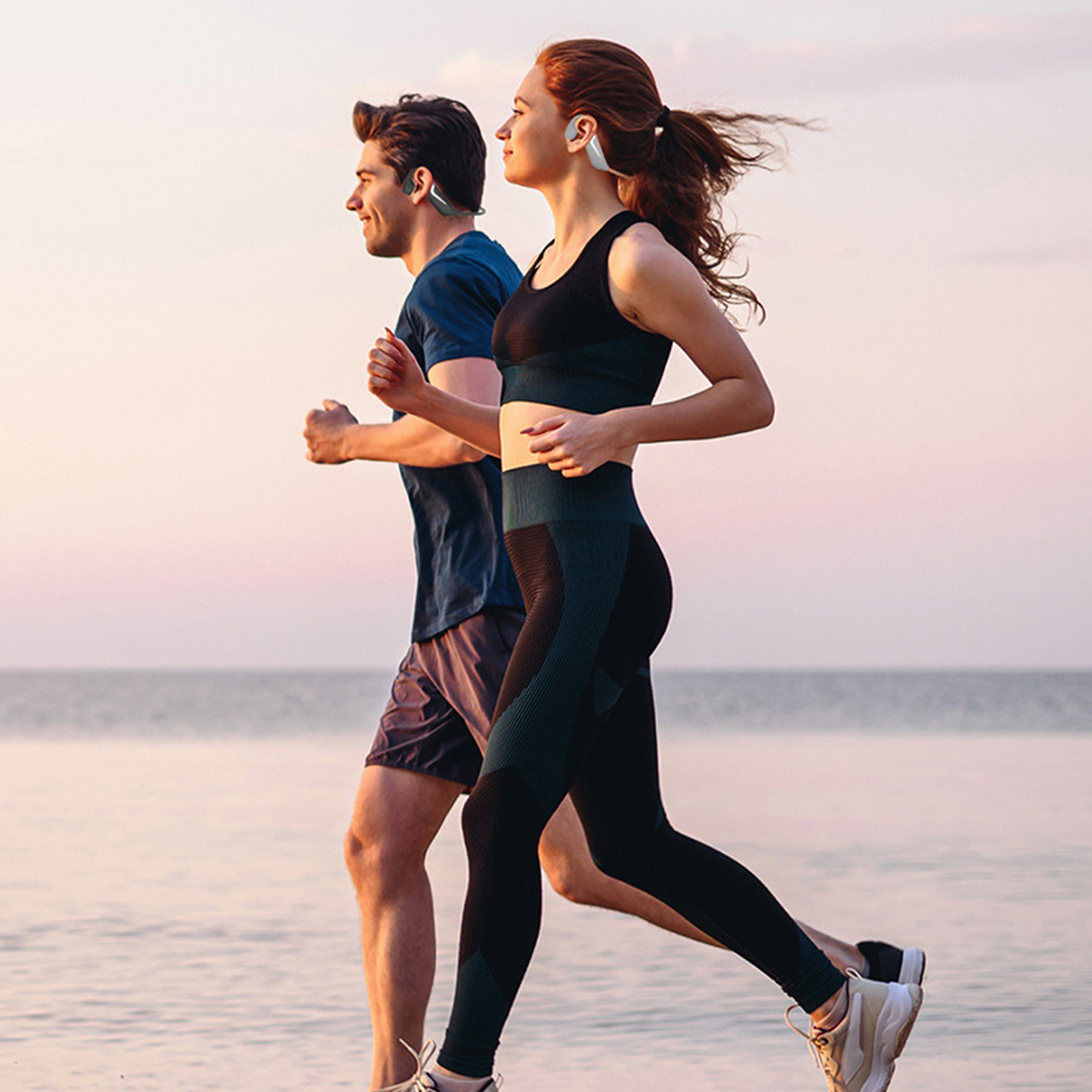 Zwei Personen laufen gemeinsam am Wasser entlang. Sie tragen Sportkleidung und haben Ohrhörer im Ohr.