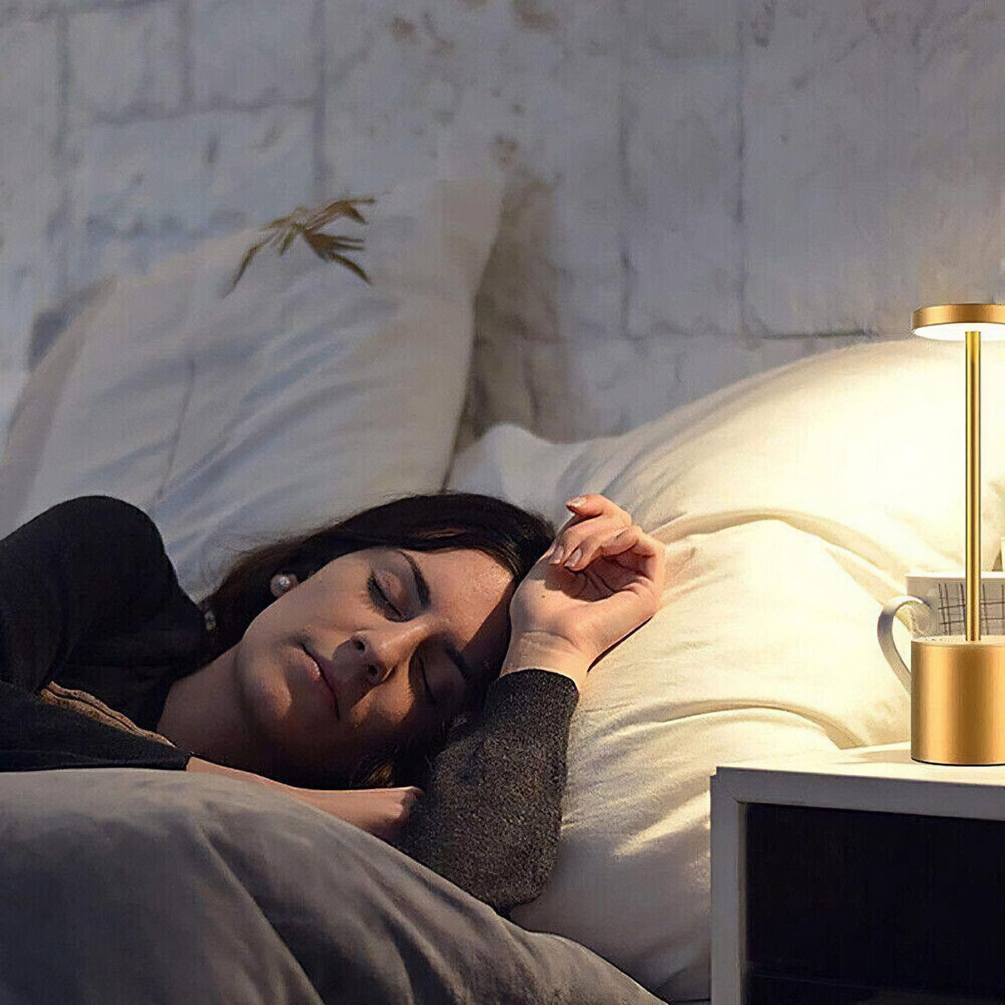 Eine Frau schläft im Bett mit goldener Nachttischlampe. Eine Tasse steht auf dem Nachttisch.