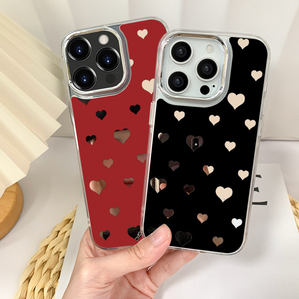 Due custodie per telefono con motivi a cuore; una rossa, una nera, tenute in mano.