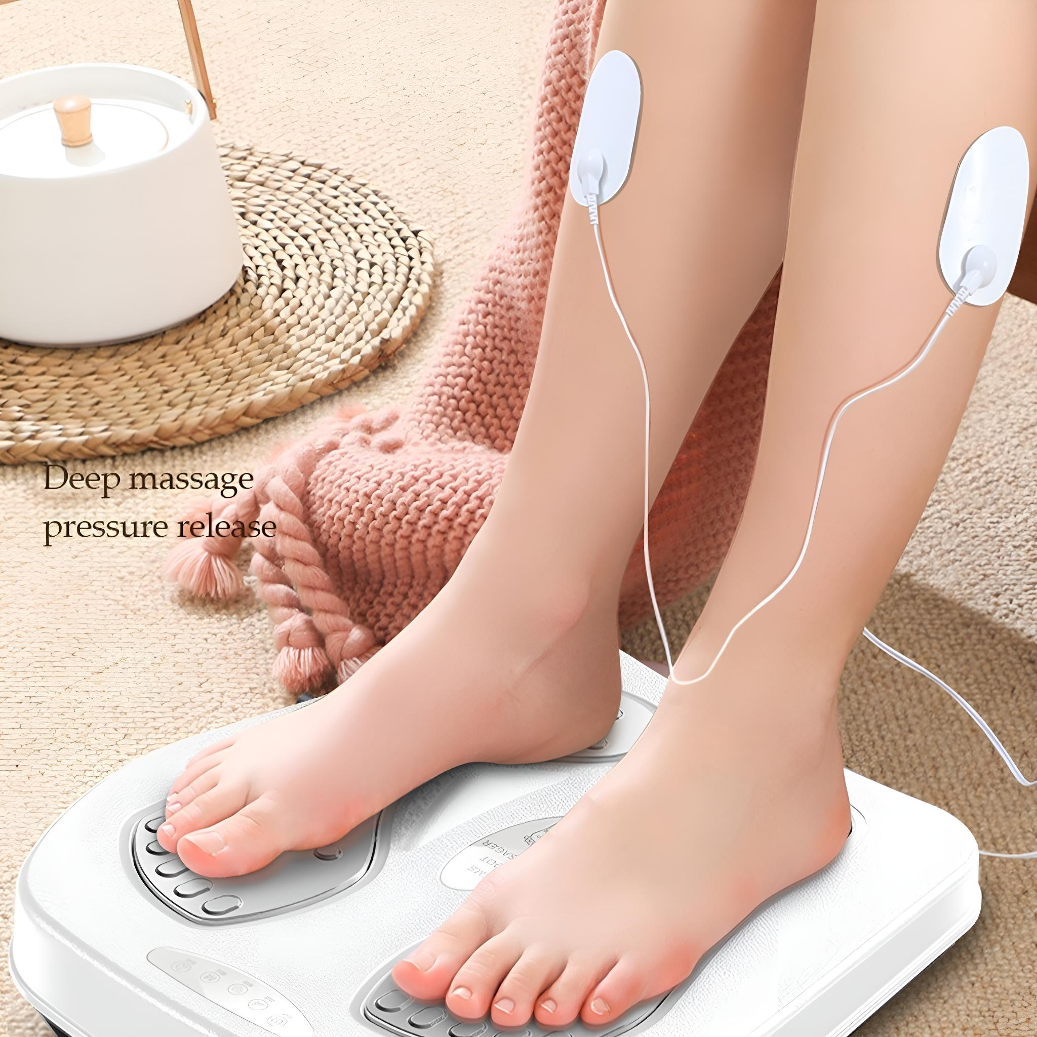 Füße auf einem Fußmassagegerät mit angebrachten Pads. Eine rosa Decke ist im Hintergrund.