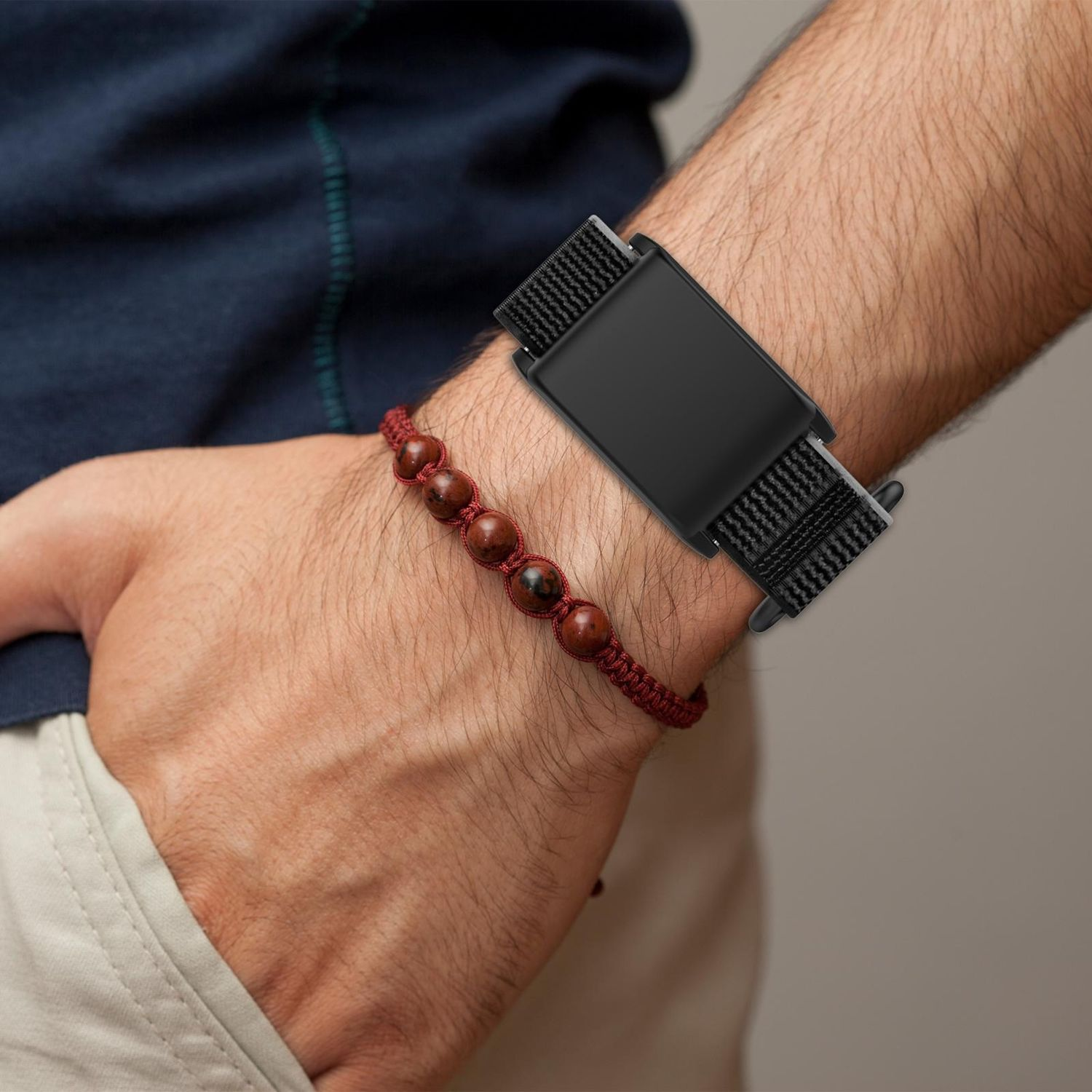 Hand eines Mannes mit einem schwarzen Fitness-Tracker-Band und einem roten Perlenarmband.