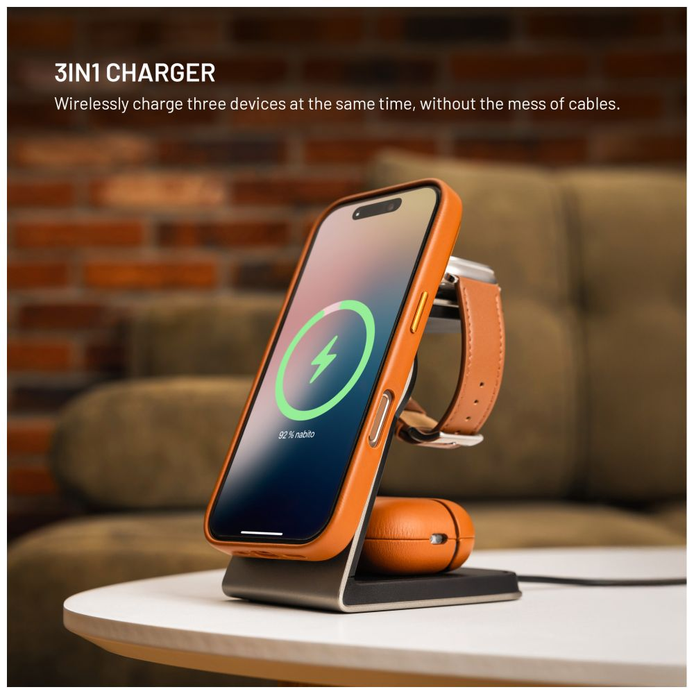 Ein 3-in-1-Wireless-Ladegerät mit Telefon, Smartwatch und Ohrhörern. Das Telefon zeigt ein Ladesymbol an. Hintergrund: Backsteinmauer und Sofa.