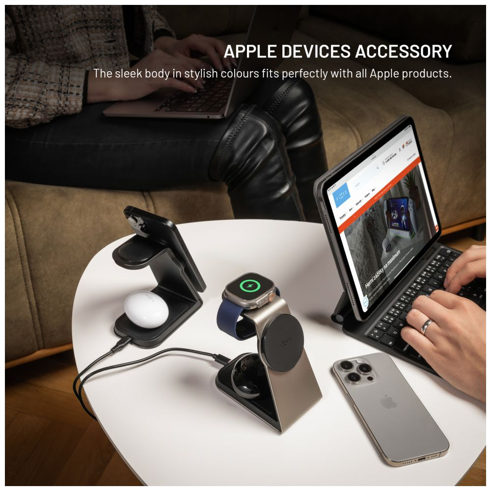 Apple-Geräte-Zubehör, mit Uhr, Telefon und Tablet auf einem weißen Tisch. Eine Person tippt auf der Tastatur des Tablets.