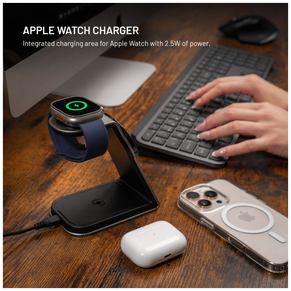Eine Apple Watch liegt auf einer Ladestation mit einem iPhone, AirPods und einer Tastatur im Hintergrund.