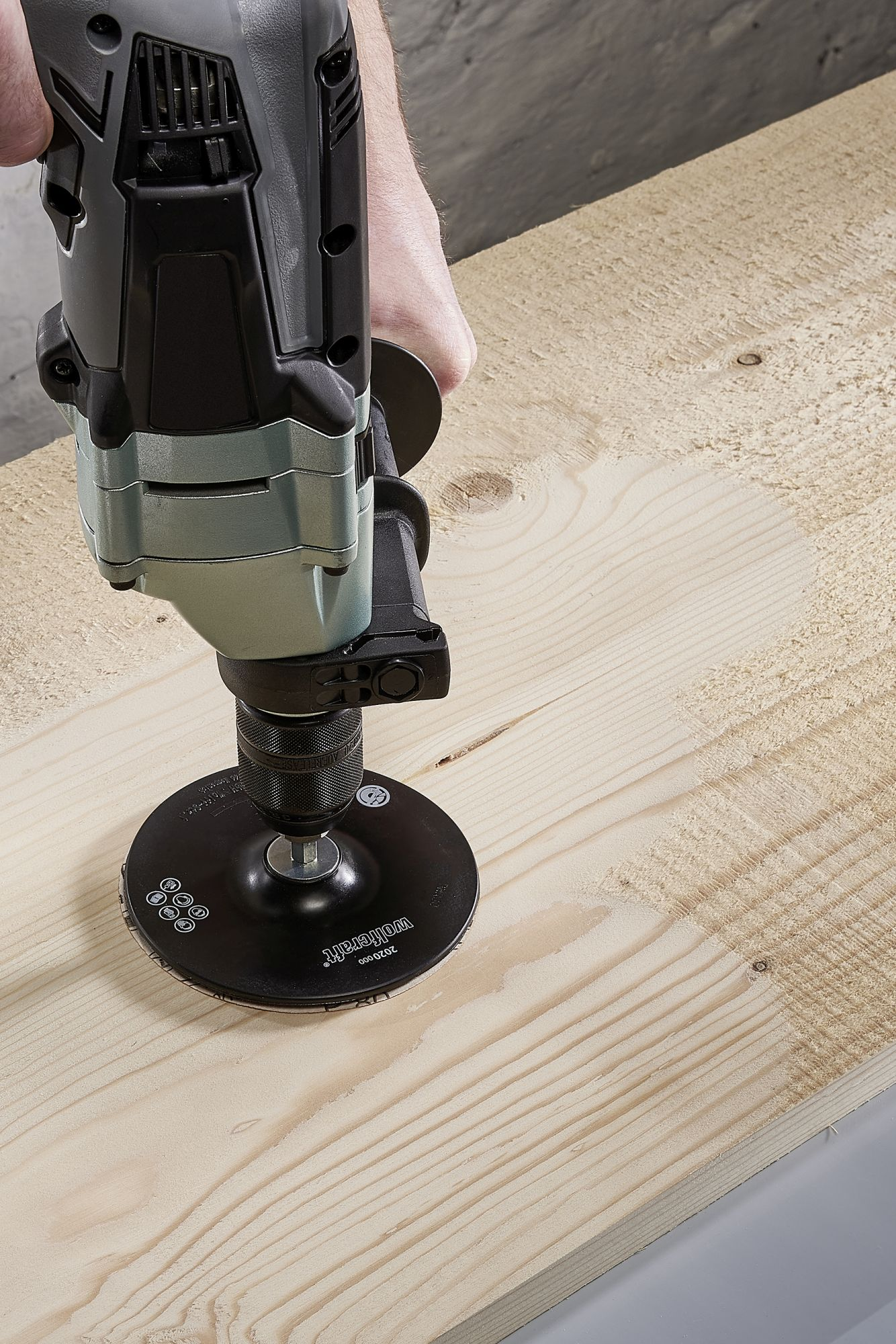 Elektrowerkzeug schleift Holz. Ein schwarzer Scheibenschleifer wird auf einer Holzoberfläche verwendet.