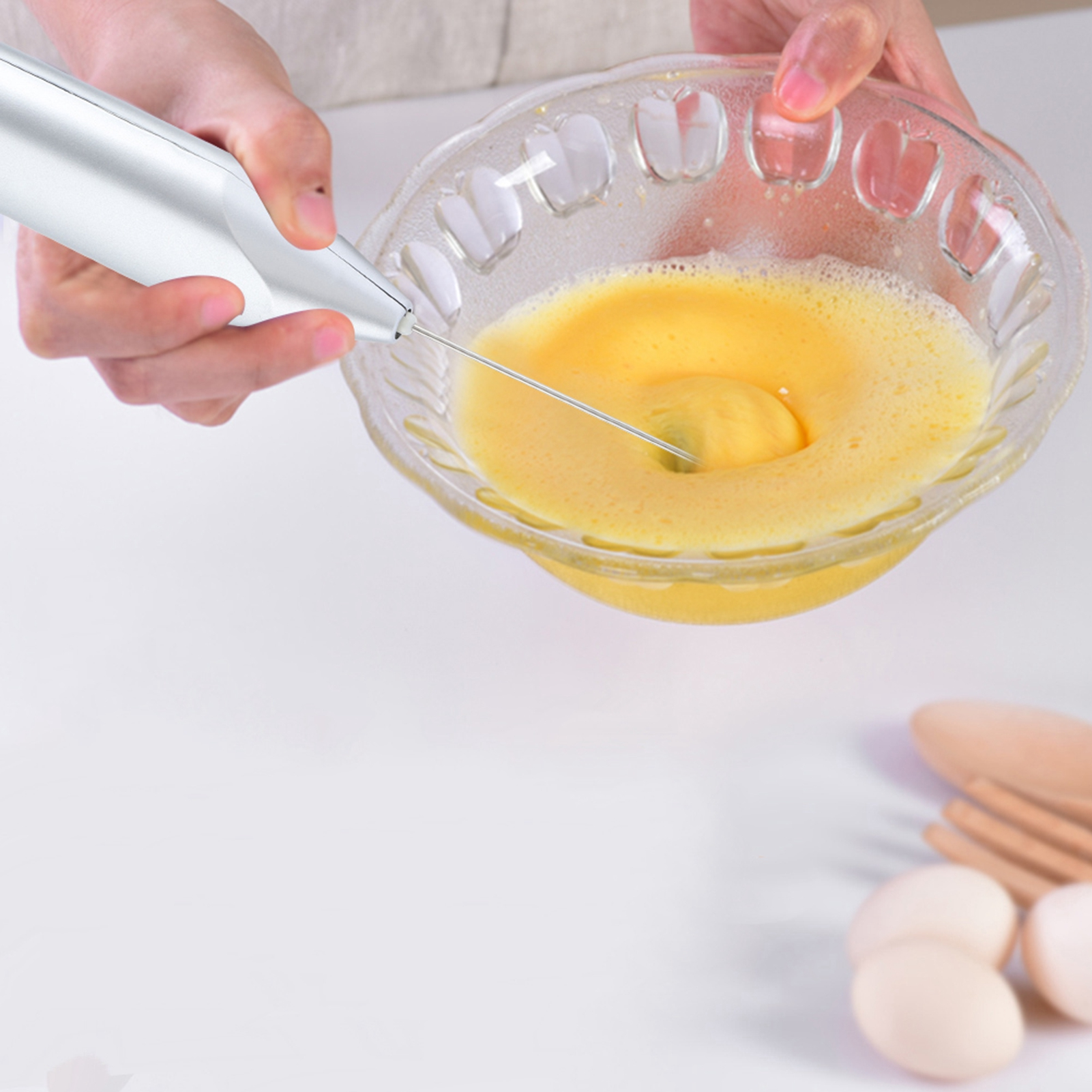 Hände halten einen silbernen Milchaufschäumer in einer Schüssel mit gelber Flüssigkeit.