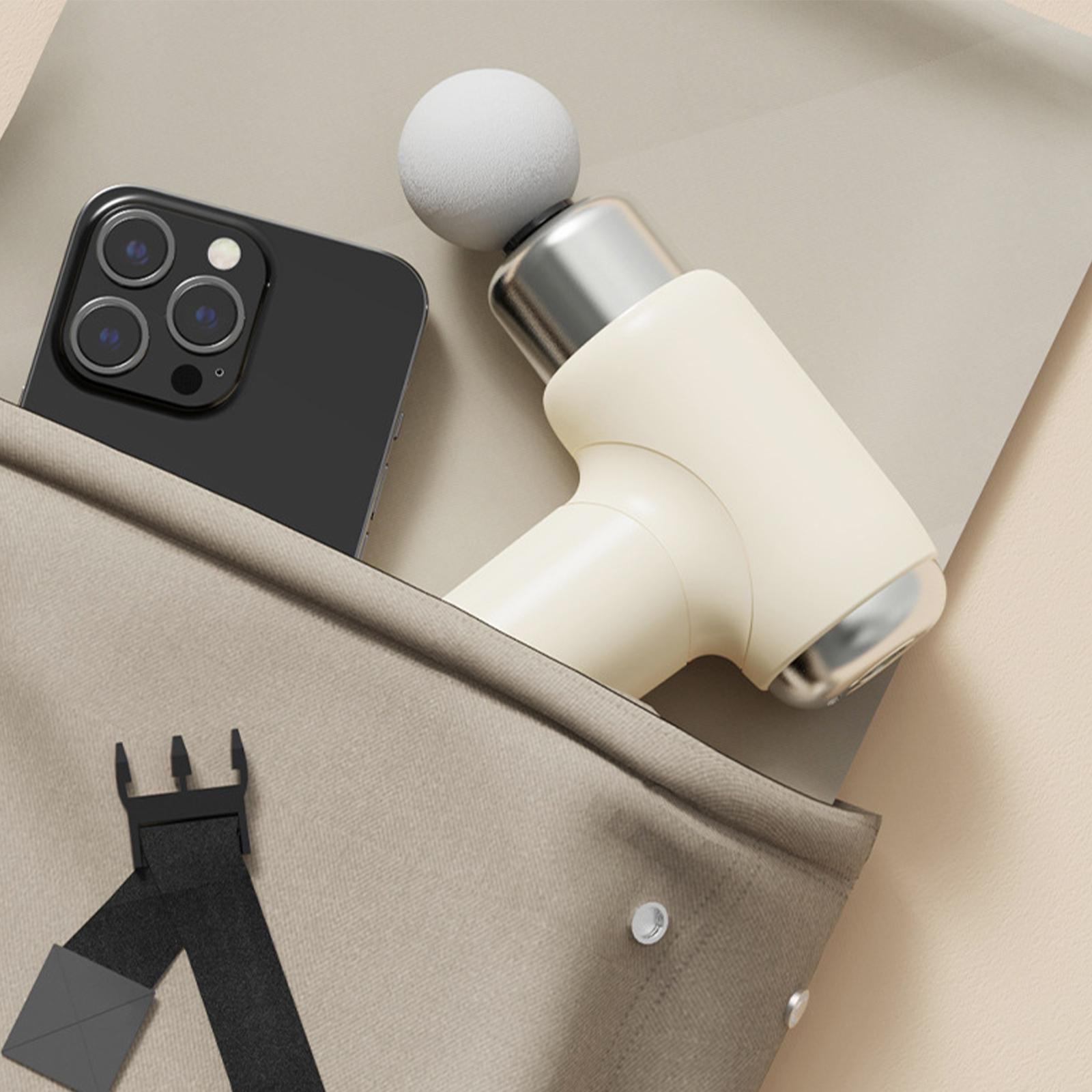Beige Tasche mit schwarzem Telefon und weißer Massagepistole innen auf beiger Oberfläche.