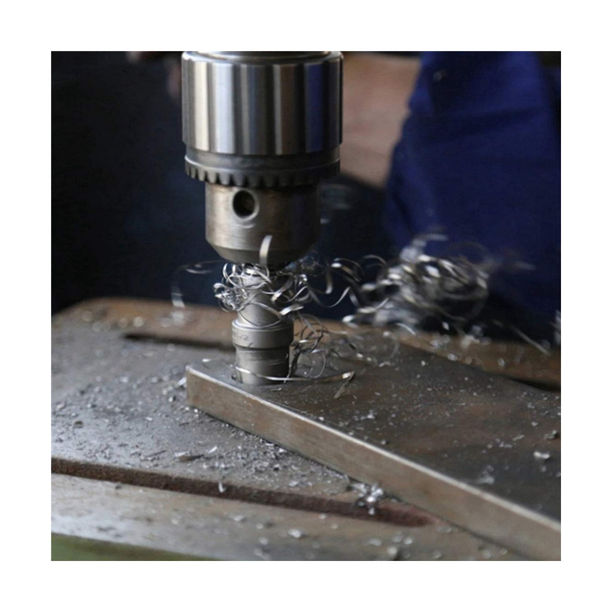 Ein Bohrer bohrt in einen Metallstab und erzeugt Metallspäne. Der Bohrer ist silberfarben.
