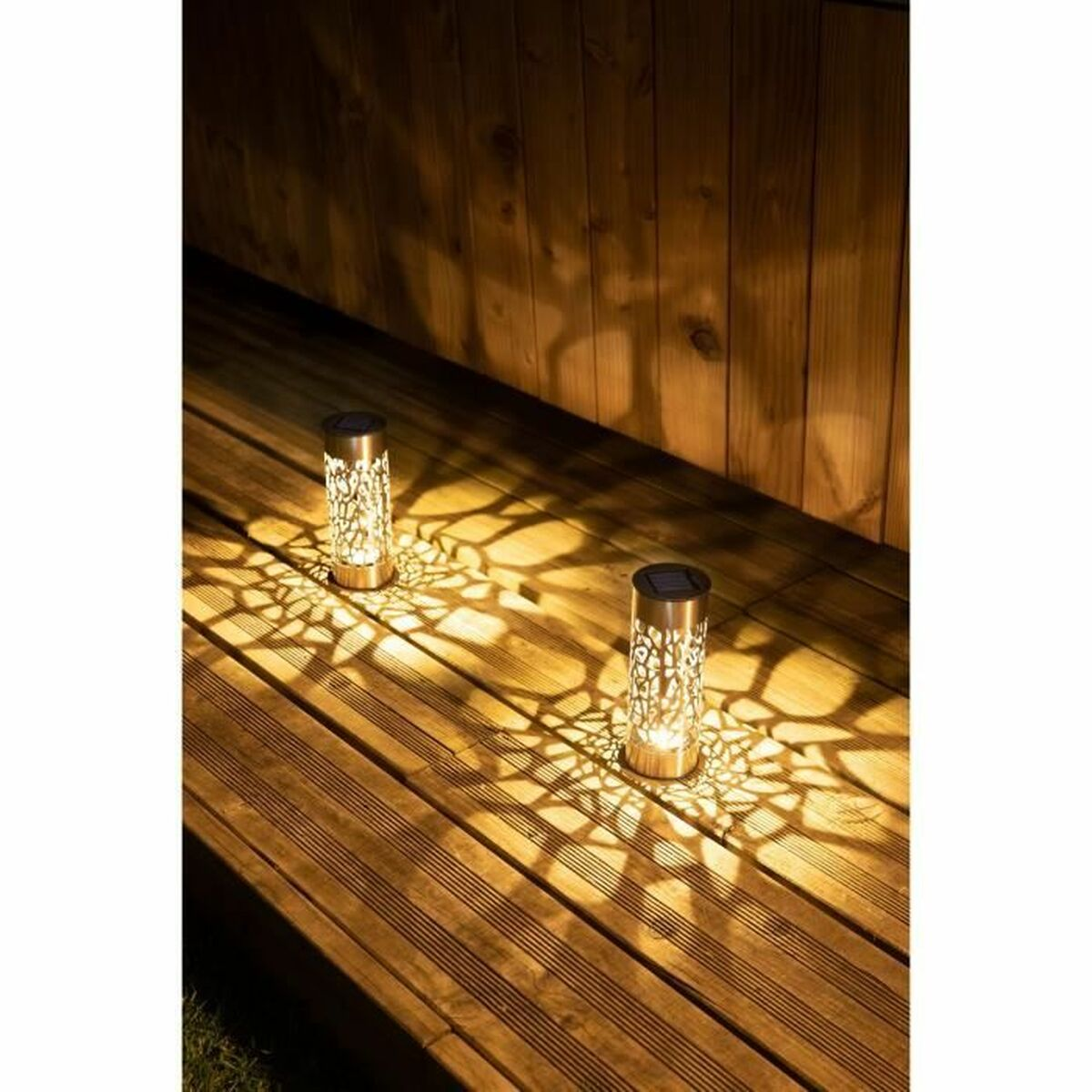 Zwei Solar-Gartenleuchten auf einem Holzdeck, die ein gemustertes Licht werfen.