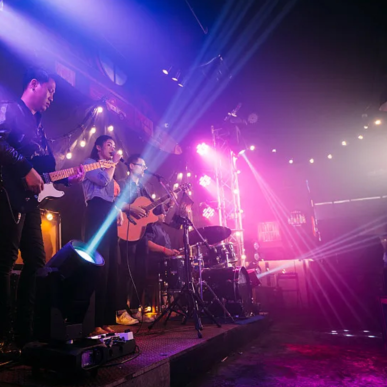 Band spielt live auf der Bühne mit Licht. Musiker spielen Gitarren und Schlagzeug unter Bühnenlicht.