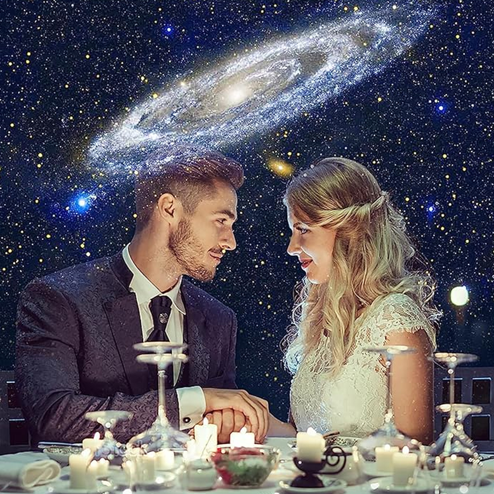 Ein Paar hält sich an den Händen an einem Tisch bei Kerzenlicht unter einer Galaxieprojektion.