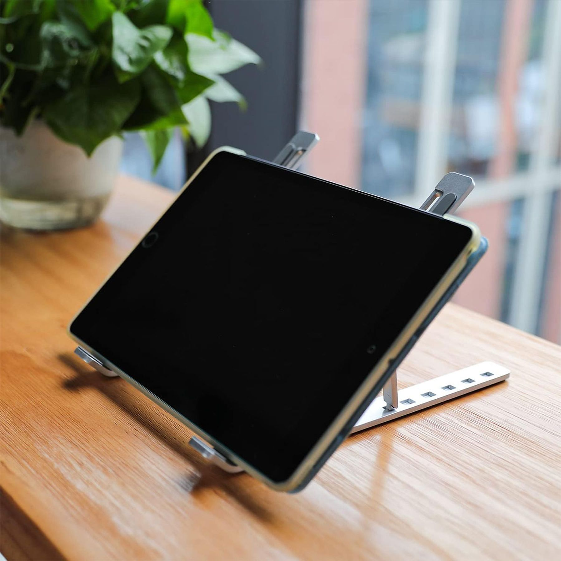Tablet auf Ständer, schwarzer Bildschirm. Holztisch, grüne Pflanze im Hintergrund. Angeschrägte Nahaufnahme.