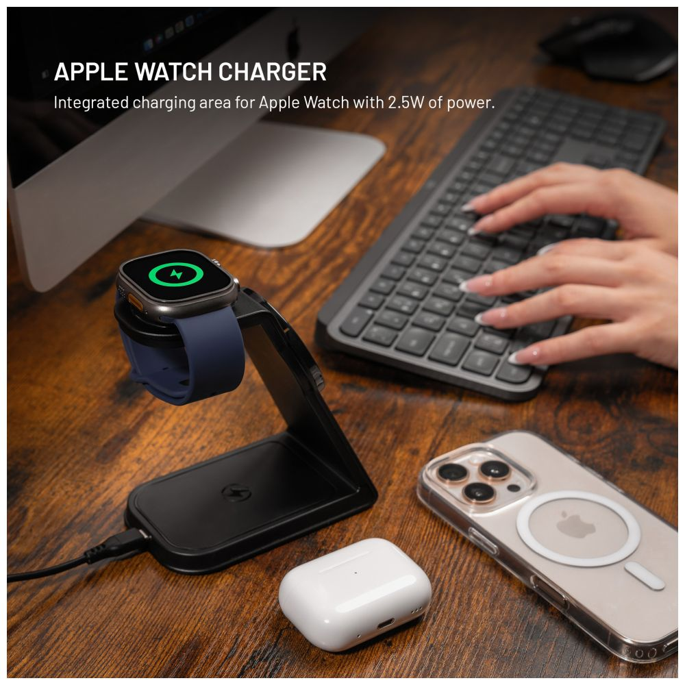 Apple Watch wird auf einem schwarzen Ständer geladen. Telefon und AirPods liegen auf dem Tisch.