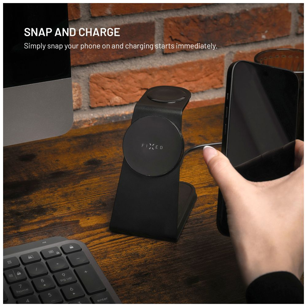 Ein schwarzer Ladeständer mit einem Telefon darauf und eine Tastatur auf einem Schreibtisch.