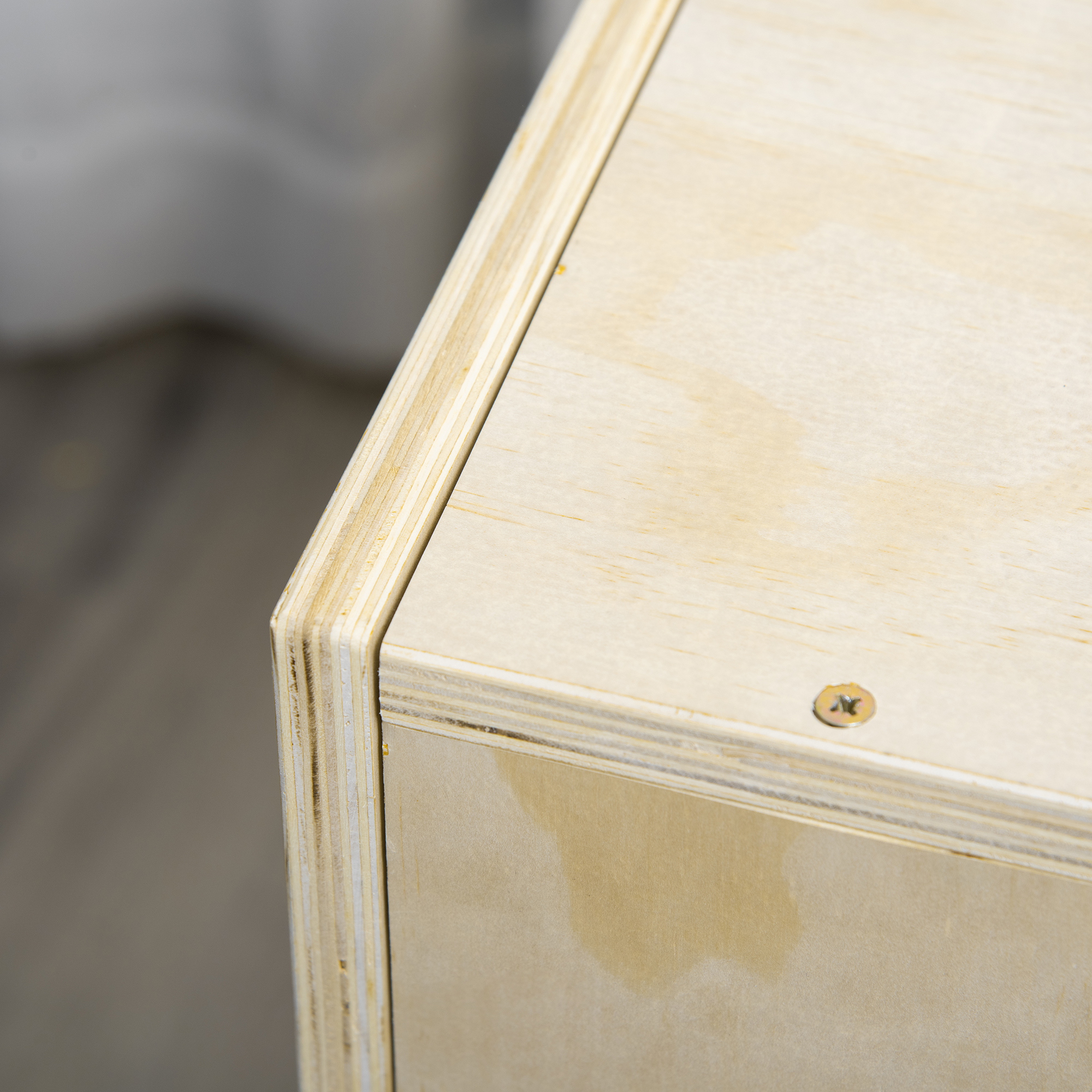 Primer plano de una esquina de caja de madera, mostrando la veta de la madera en capas y una cabeza de tornillo.
