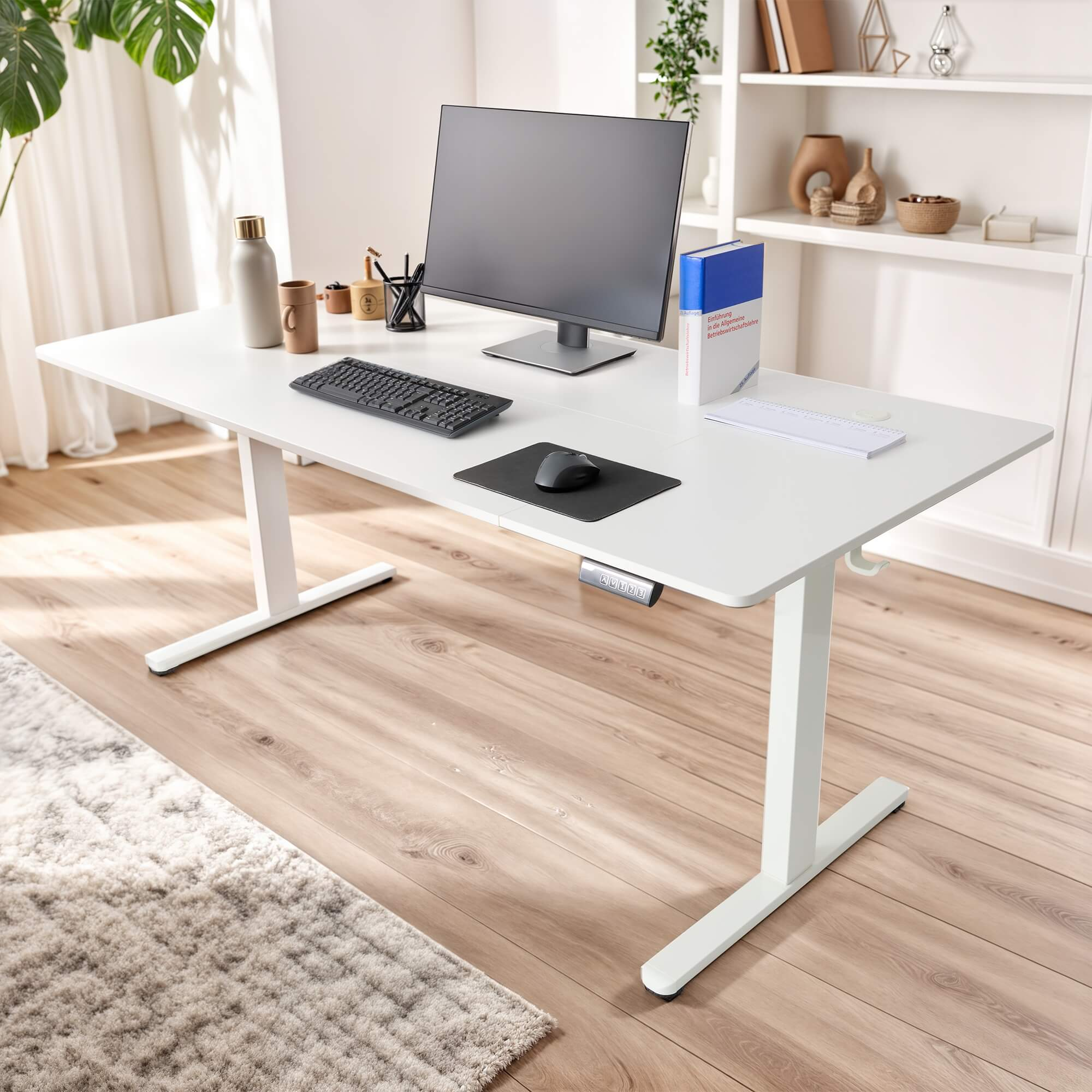 Ein weißer, höhenverstellbarer Schreibtisch mit Monitor, Tastatur und Büromaterialien.
