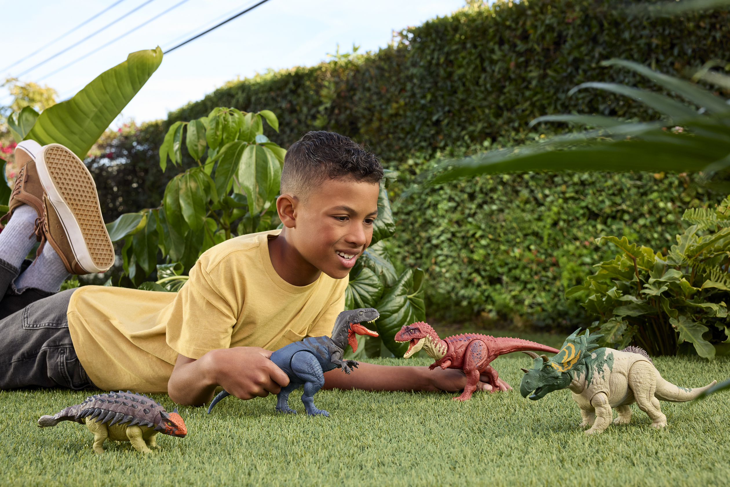 Ragazzo sdraiato sull'erba, gioca con dinosauri giocattolo, sfondo verde.