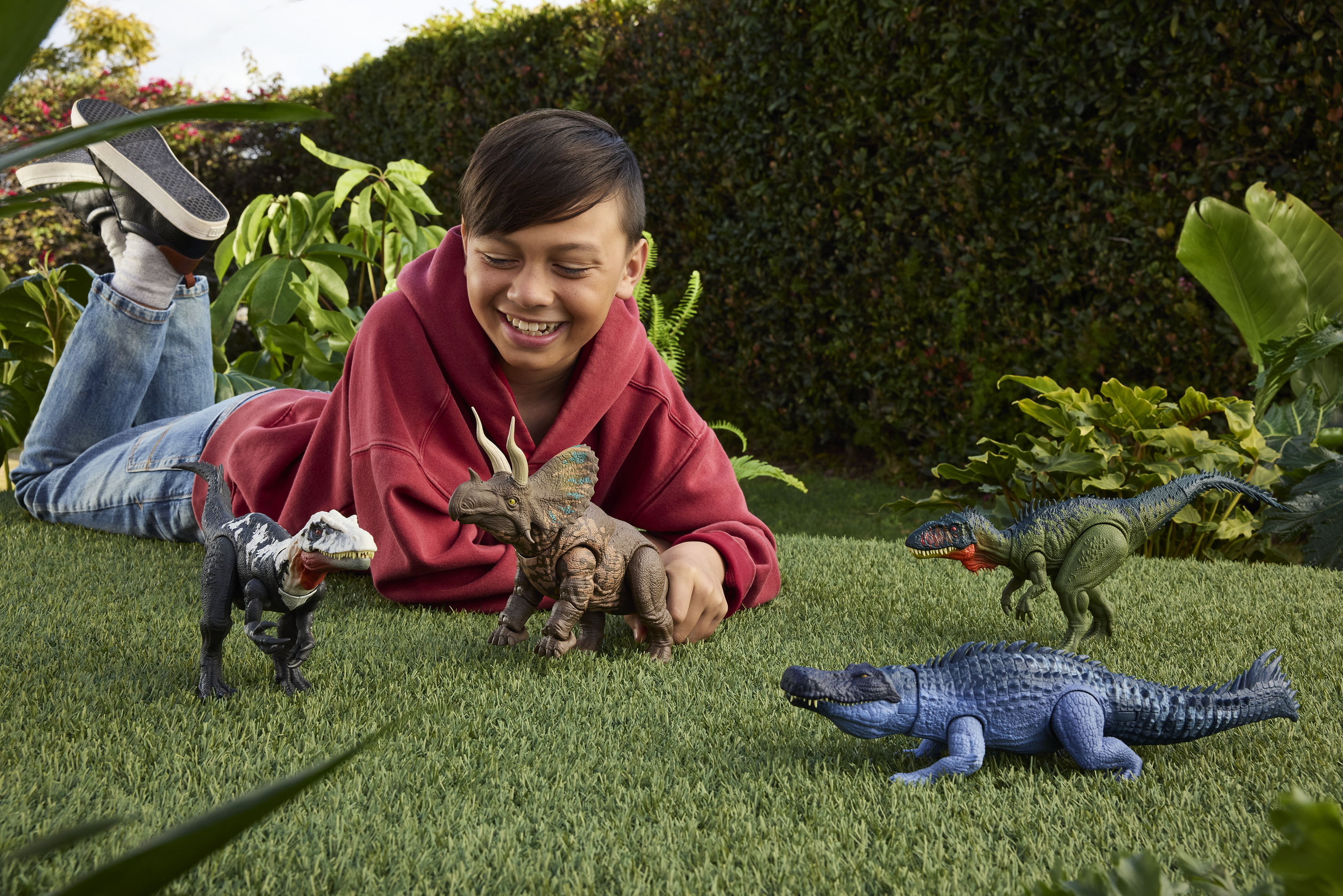 Un niño jugando con dinosaurios de juguete en un césped verde.
