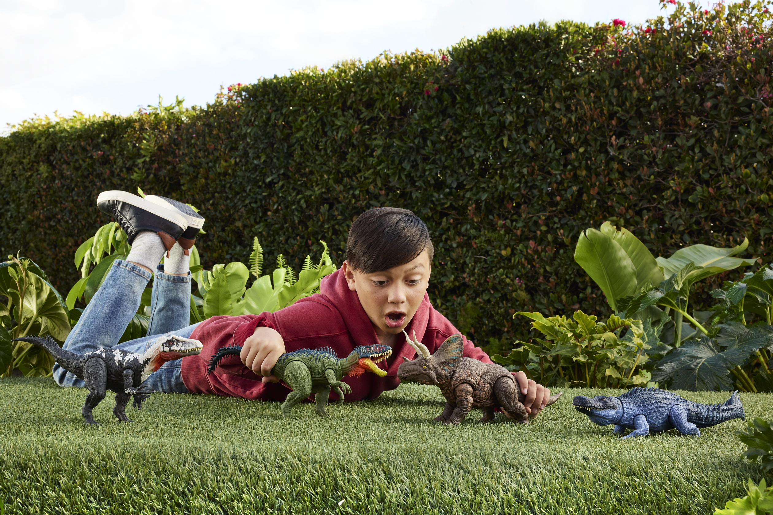 Un niño está acostado en la hierba jugando con dinosaurios de juguete. Varios dinosaurios están dispersos a su alrededor.