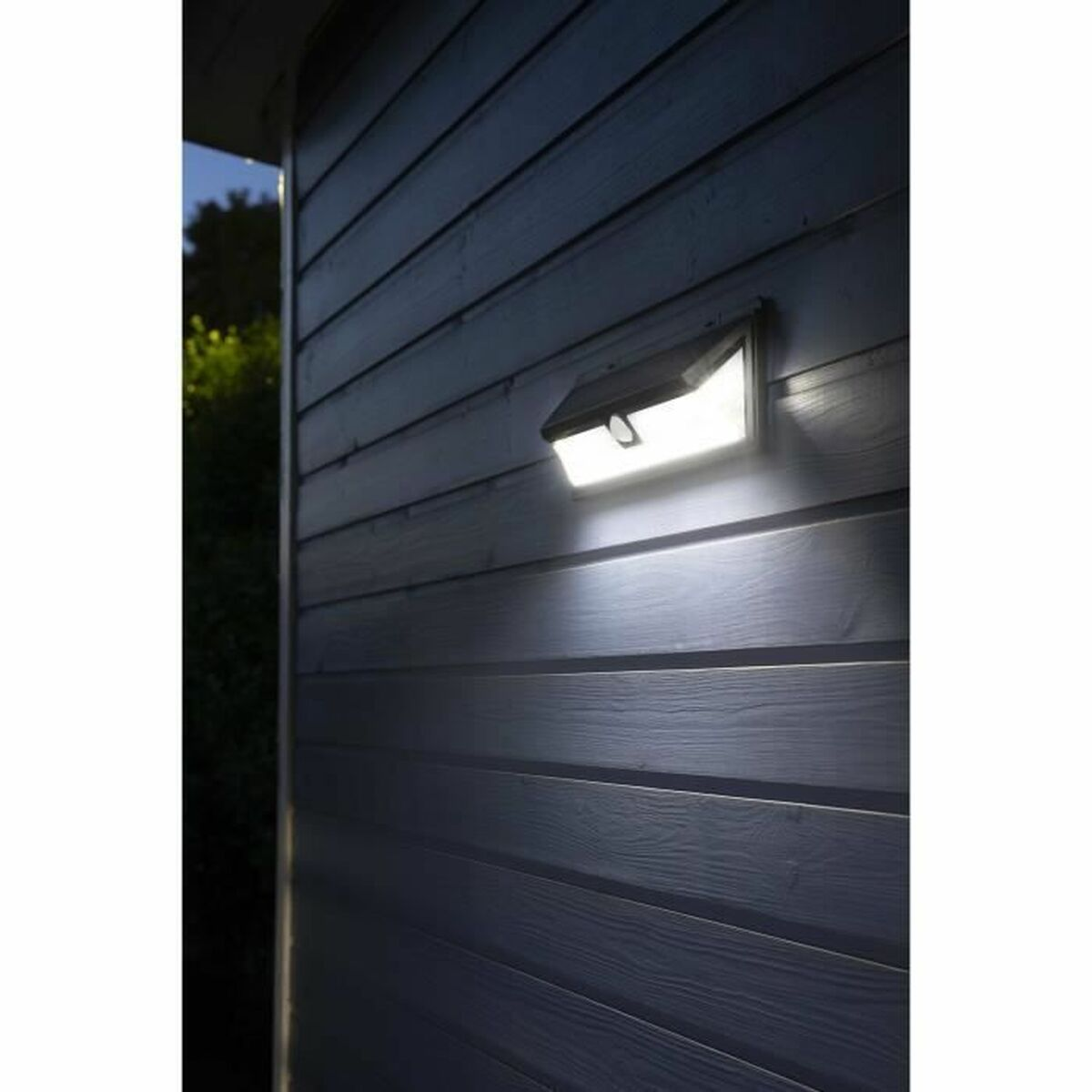 Ein schwarzes Solarlicht ist an einer Holzwand montiert. Das Licht ist an.