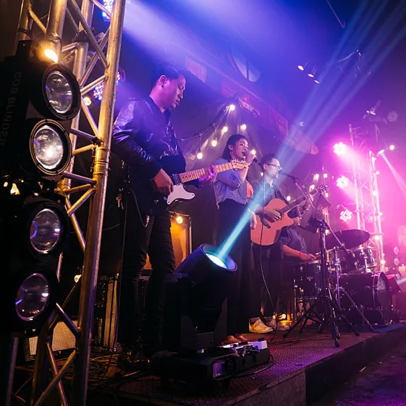 Band spielt auf der Bühne unter Scheinwerfern. Lichter scheinen auf Bandmitglieder und Publikum.
