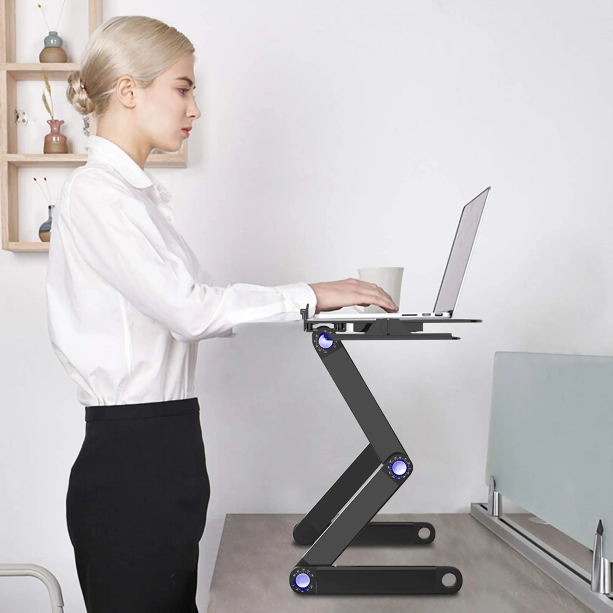 Frau benutzt Laptop auf schwarzem, verstellbarem Schreibtisch, im Büro stehend.